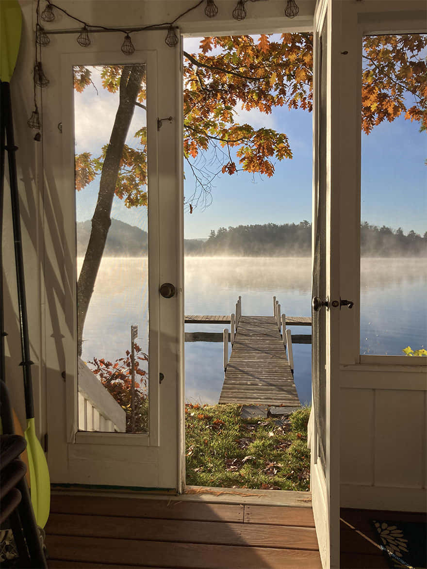 Beautiful Lake 桌布 壁紙 — 敞開的門框住一個霧氣瀰漫的秋日湖泊，木製碼頭延伸至平靜的水面，上方是清澈的藍天。