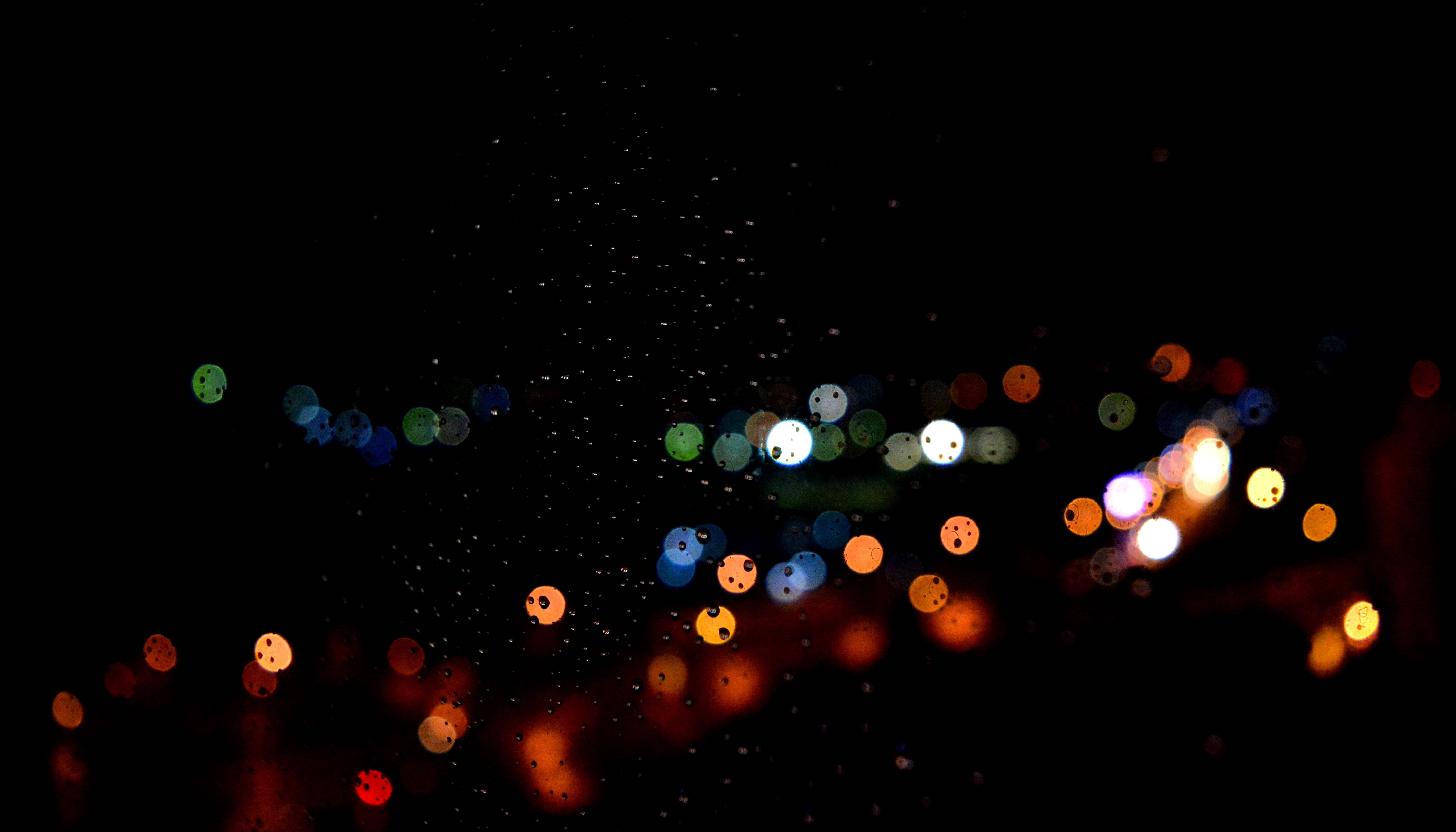 黑色 桌布 壁紙 — 散景光線劃過漆黑的夜空，雨滴捕捉到色彩繽紛的城市光芒。