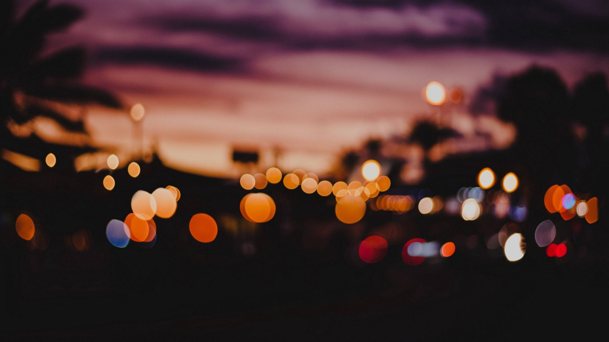 Bokeh 桌布 壁紙 — 散景燈光在暗紫色的天空下溫暖地發光，城市交通模糊成柔和的光球。