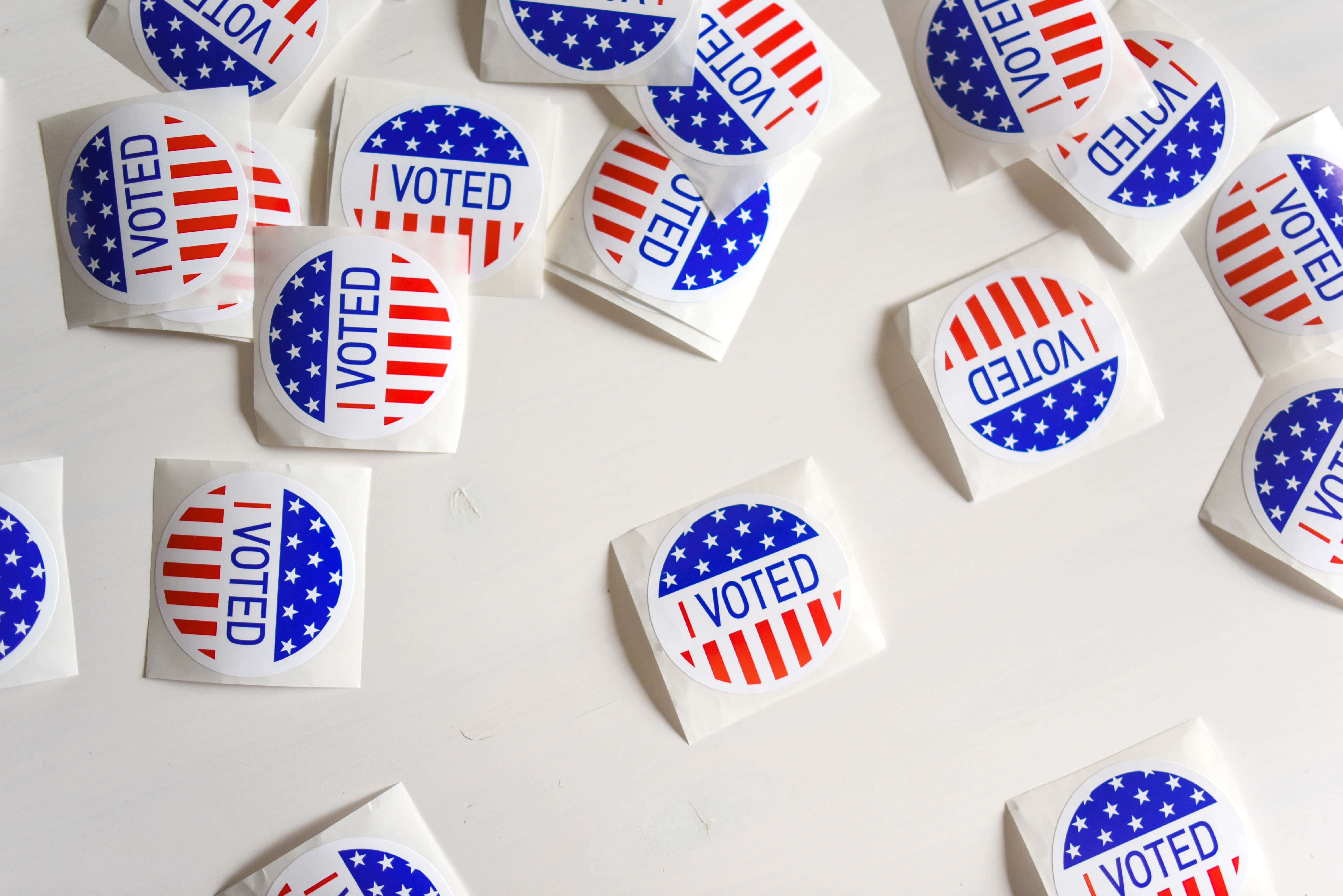 Election 桌布 壁紙 — 散落的「我投了票」貼紙，帶有美國國旗設計，位於純白表面上。