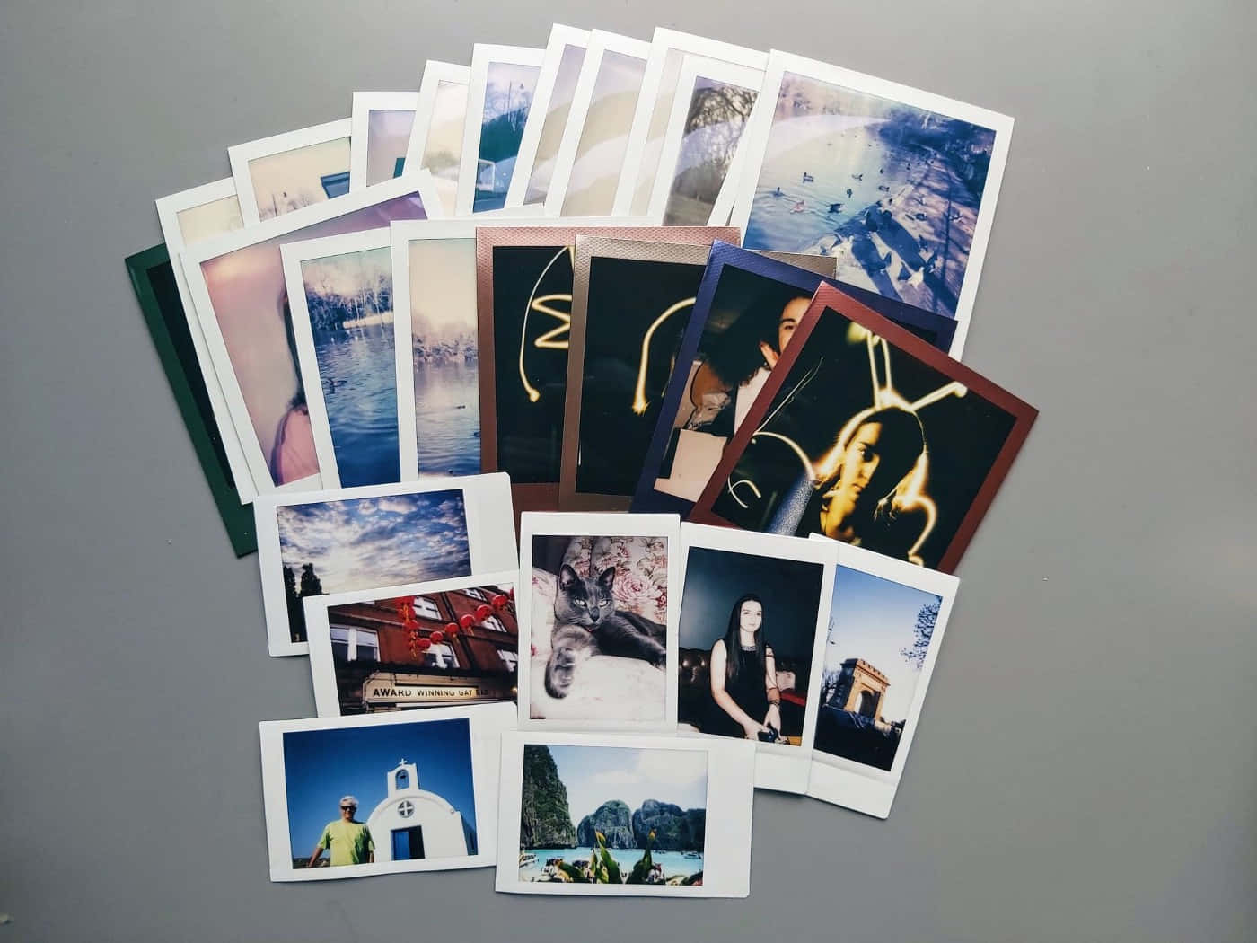 Photograph 桌布 壁紙 — 散落的拍立得照片扇，在灰色中性表面上展示多樣的旅行回憶和肖像。
