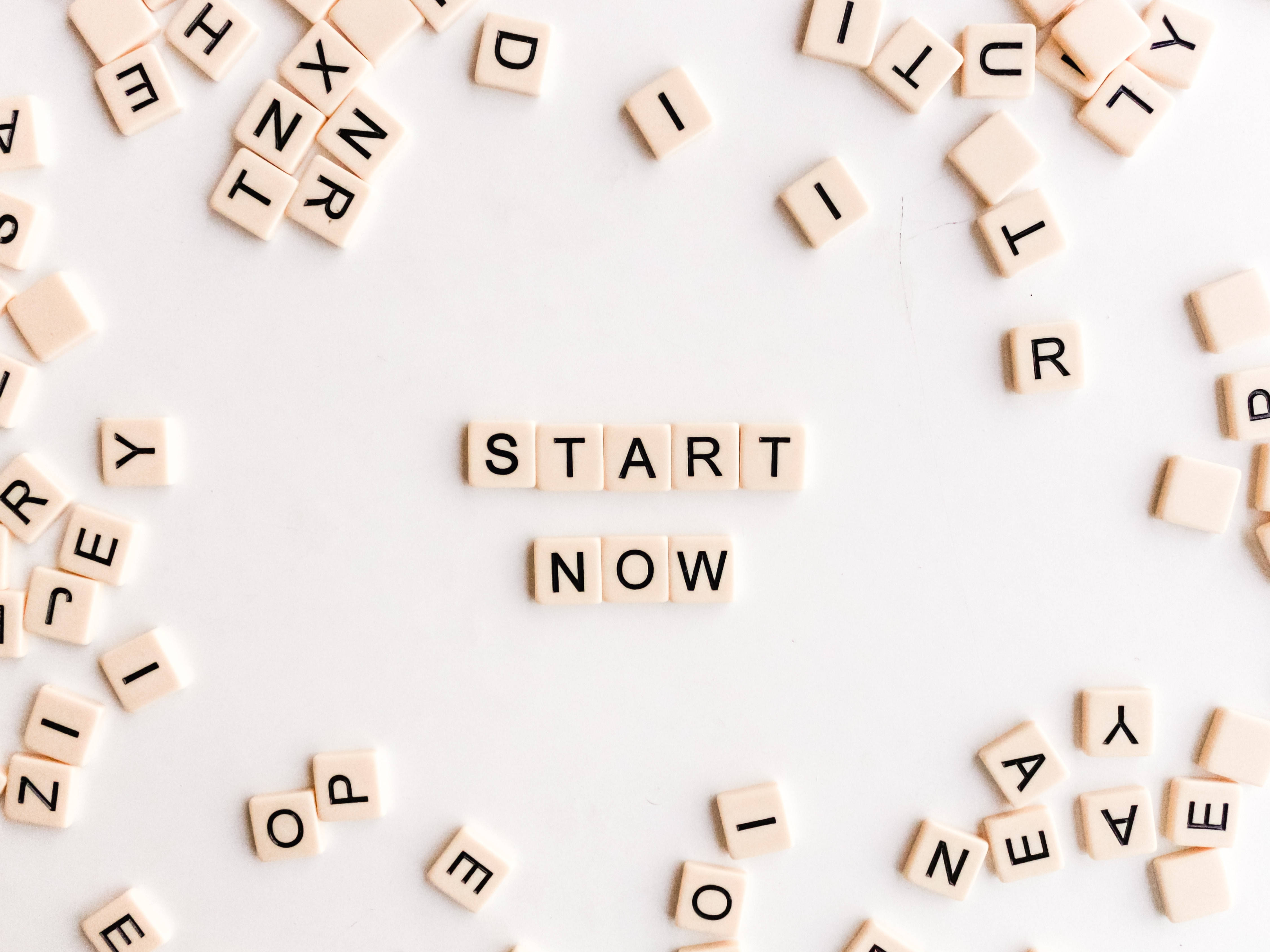 Reactions 桌布 壁紙 — 散落的米色字母瓷磚在乾淨的白色表面上居中拼出「START NOW」，周圍是隨機字母。