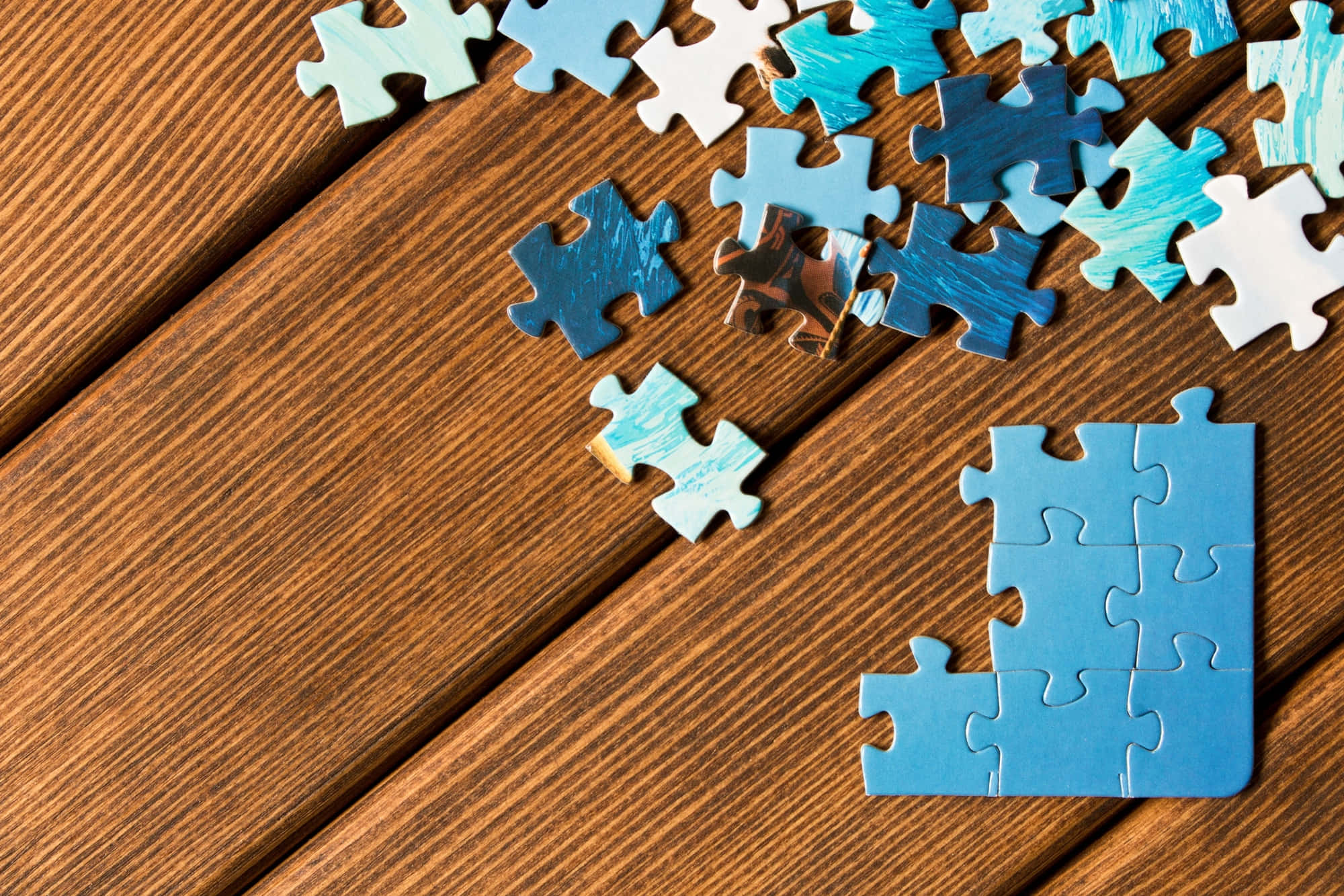 Puzzle 桌布 壁紙 — 散落的藍色和白色拼圖碎片放在溫暖的木質表面上，其中一小部分已經拼好。