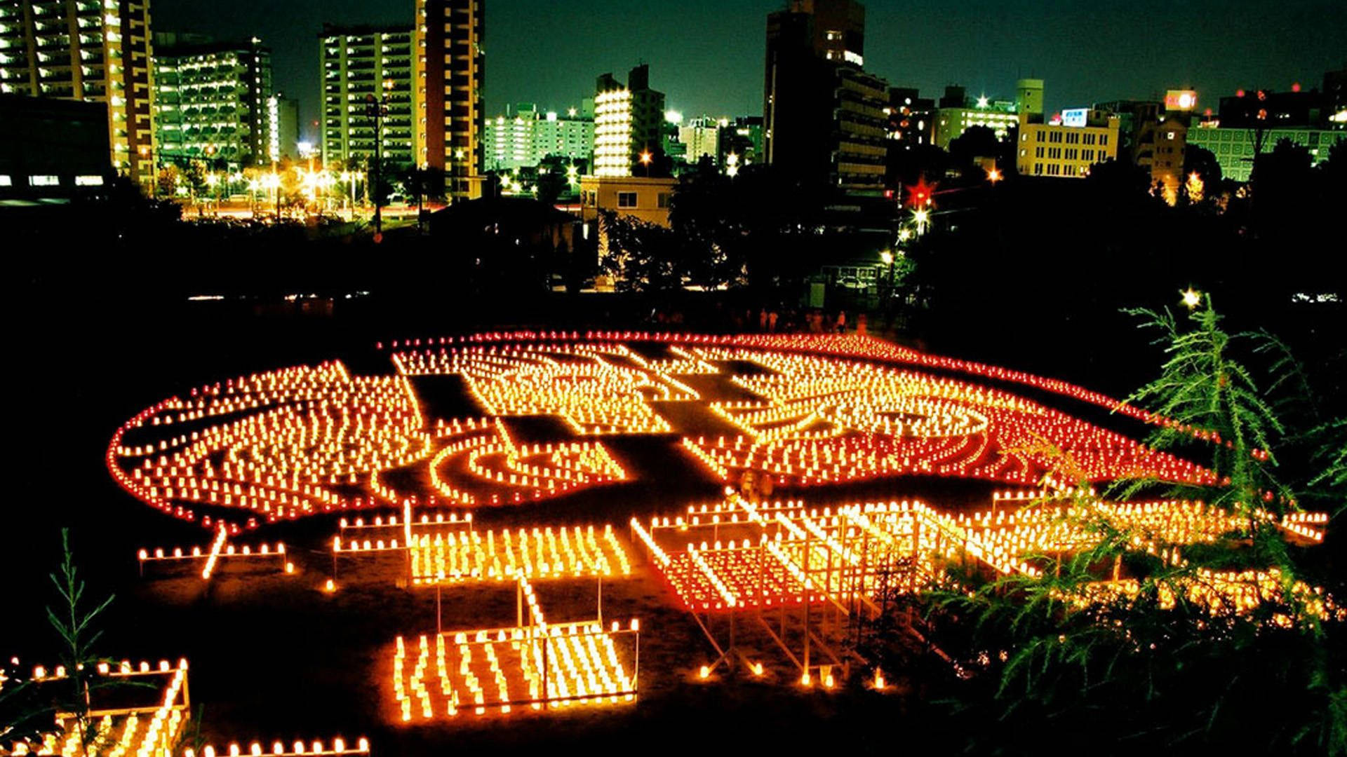Fukuoka 桌布 壁紙 — 數千支發光的蠟燭在夜晚的城市天際線下的黑暗田野中形成複雜的圖案。