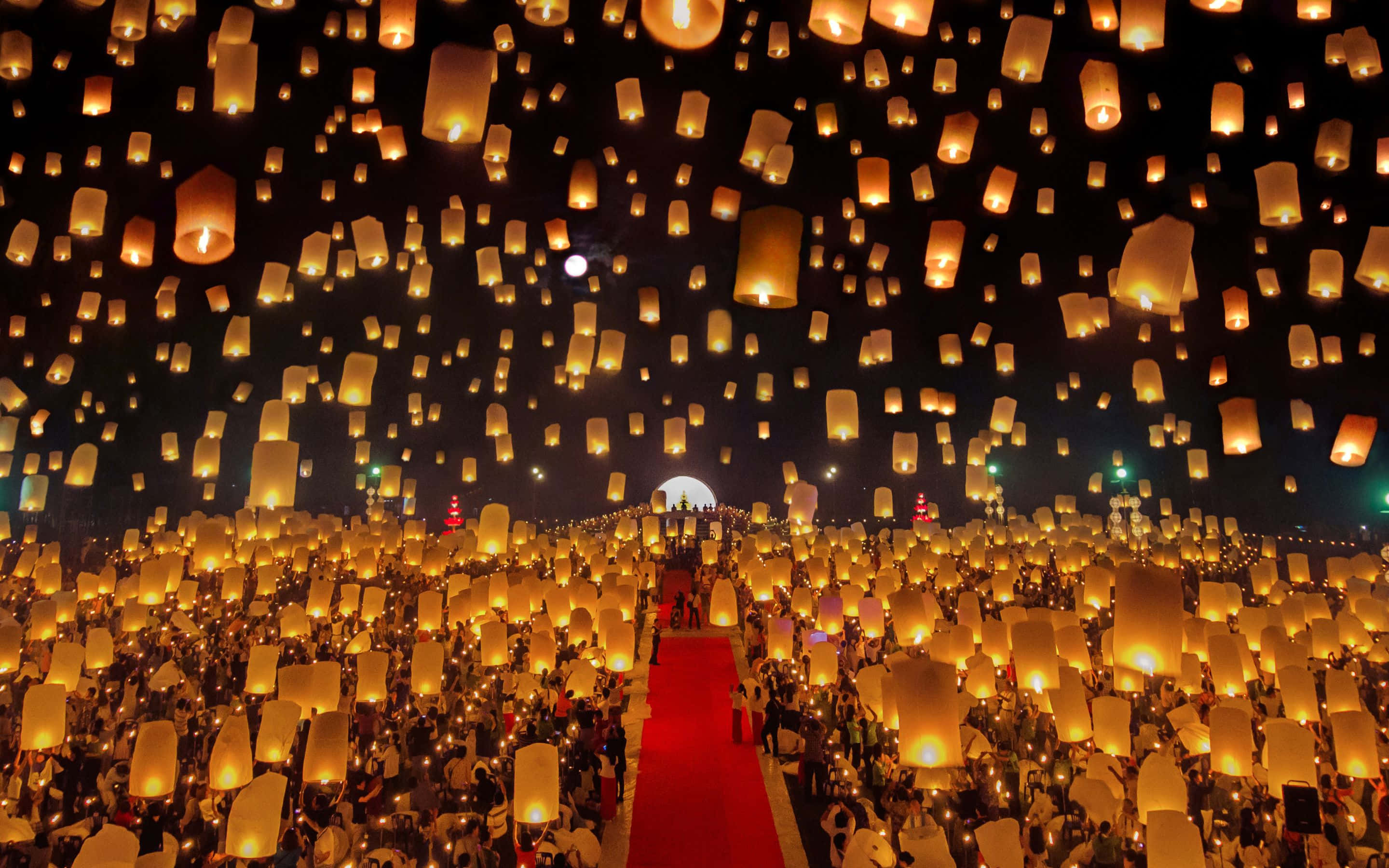 2880x1800 桌布 壁紙 — 數千盞發光的天燈從人群中升起，照亮了紅地毯路徑上方的黑暗天空。