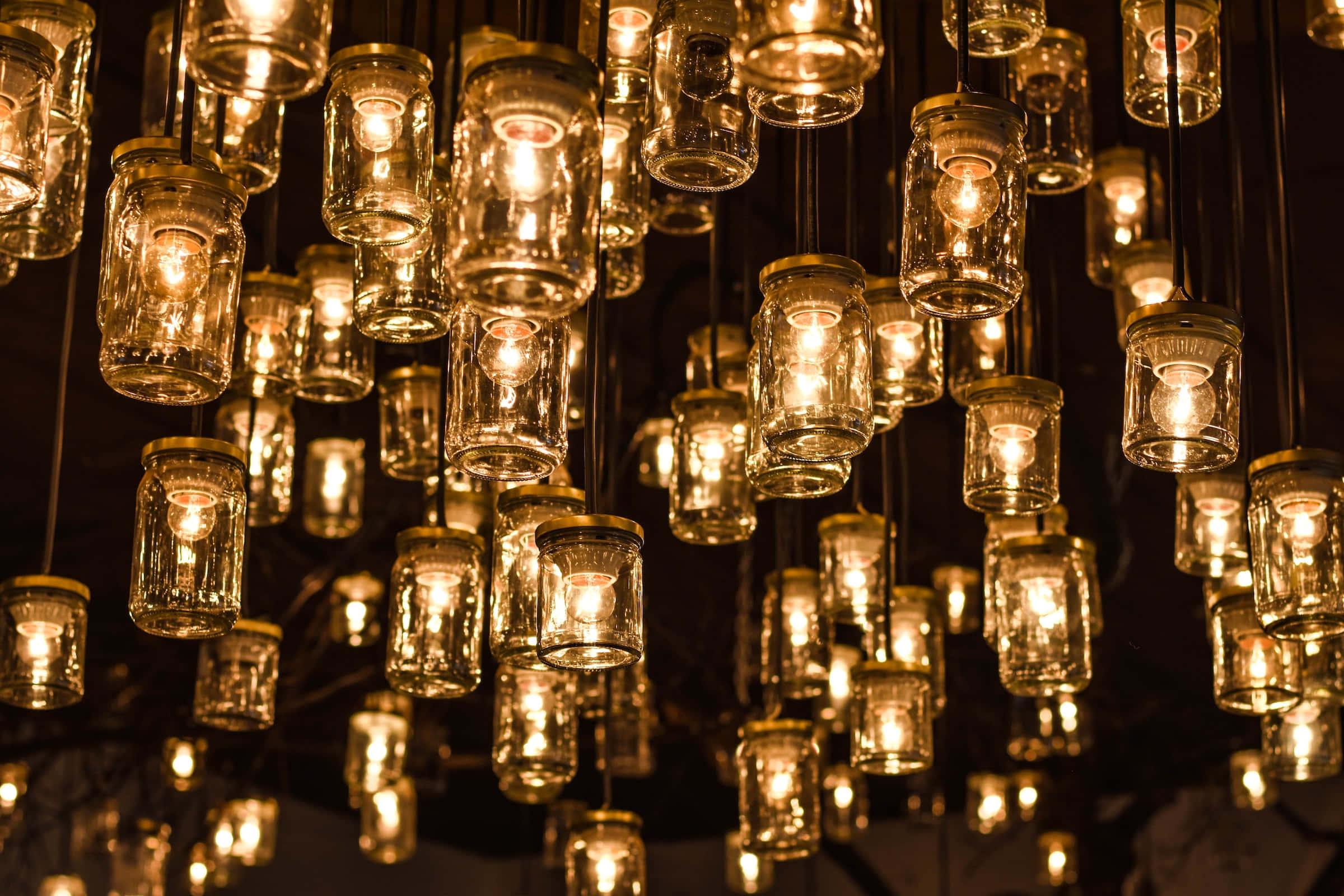 Light Bulb 桌布 壁紙 — 數百個玻璃瓶燈懸掛在溫暖的金色光芒中，映襯著深色背景。