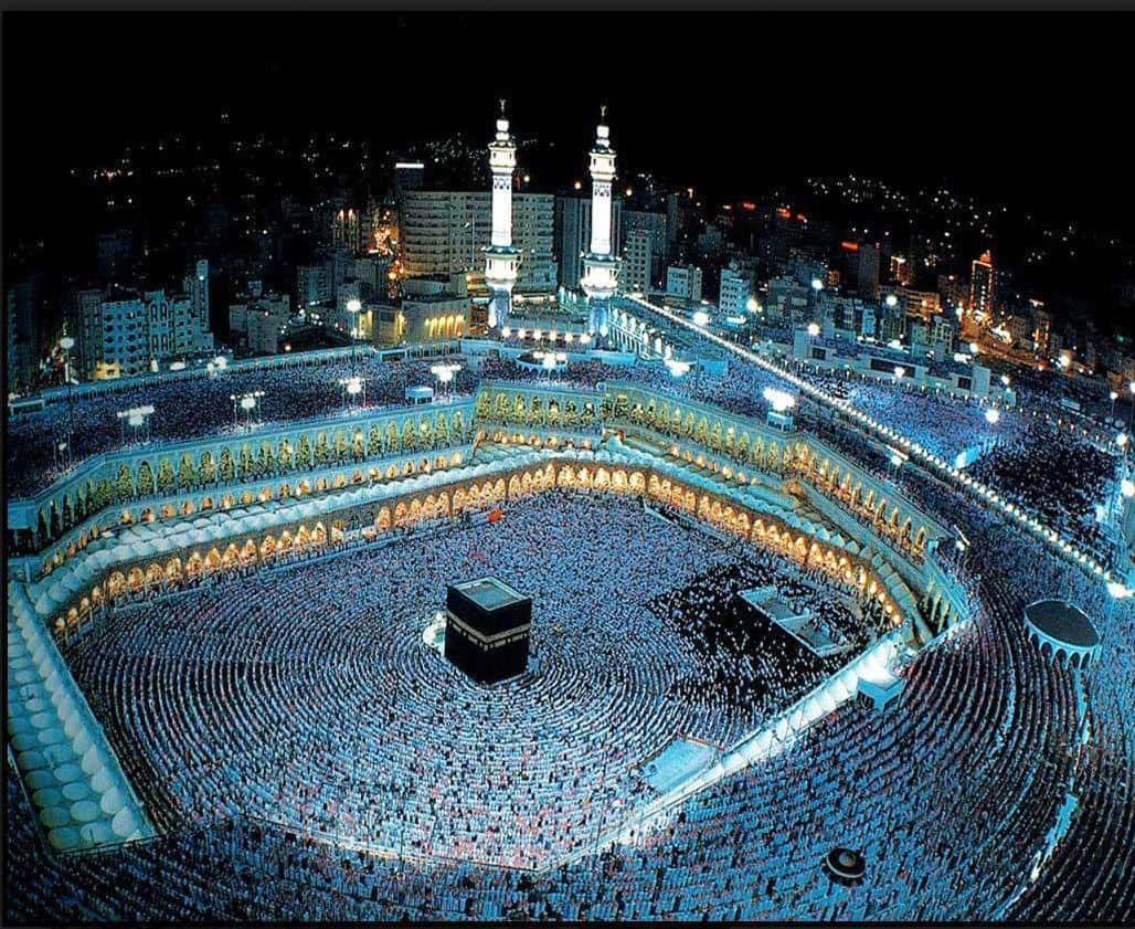 Kaaba 桌布 壁紙 — 數百萬朝聖者在明亮燈光下環繞麥加天房的夜間航拍視圖。