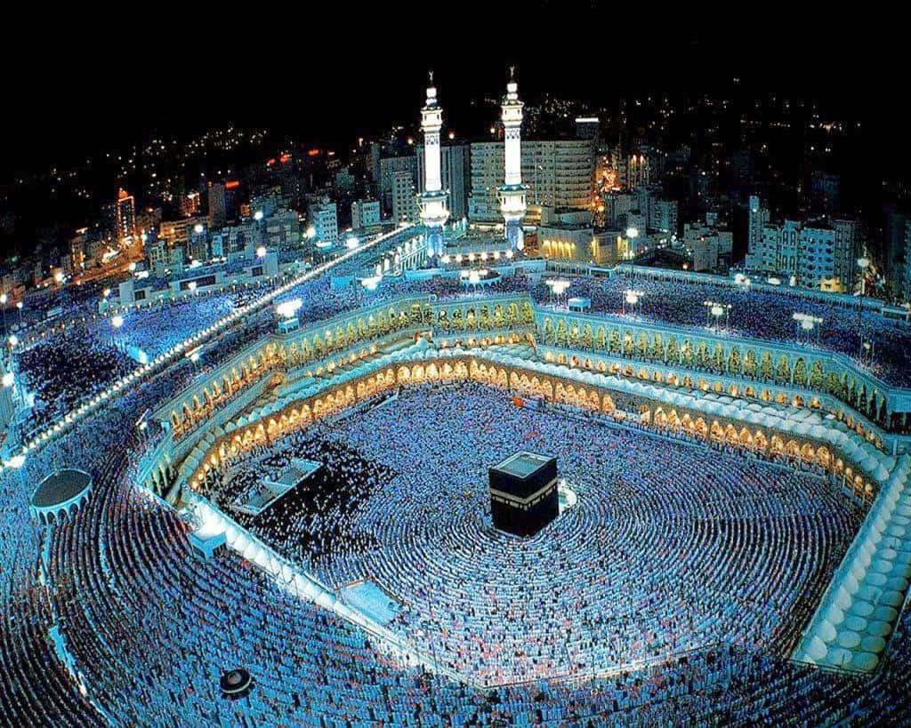 Kaaba 桌布 壁紙 — 數百萬朝聖者在明亮燈光下繞行麥加天房的空中夜景。