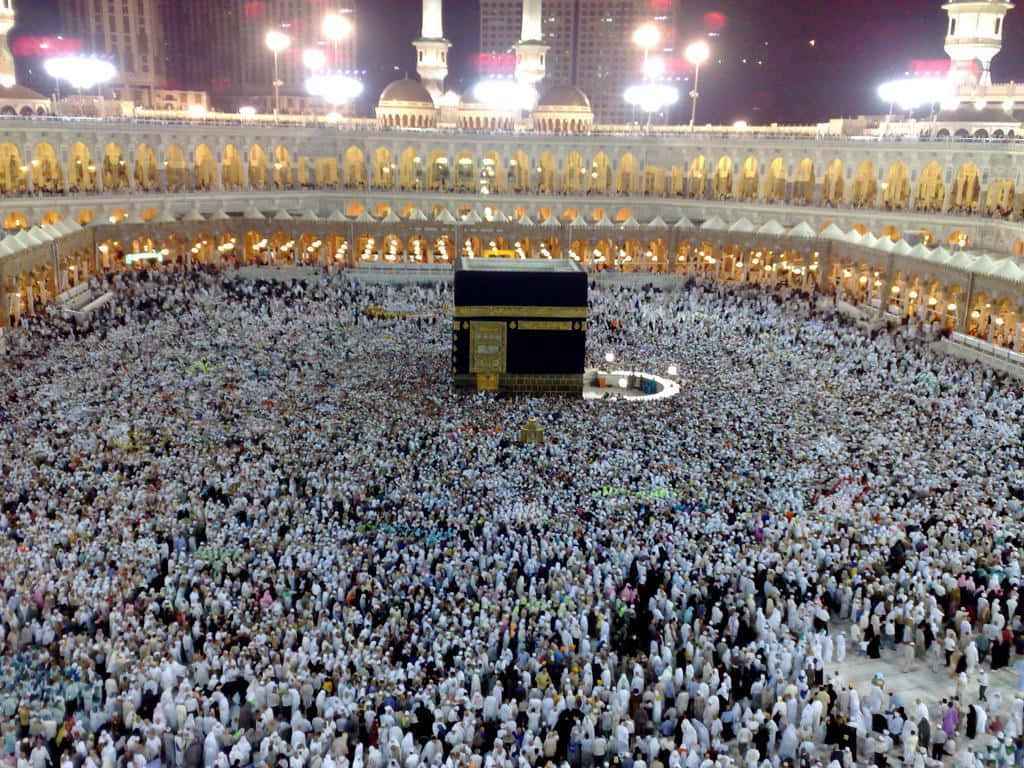 Kaaba 桌布 壁紙 — 數百萬身穿白衣的朝聖者在夜晚明亮的燈光下繞行卡巴的鳥瞰圖。
