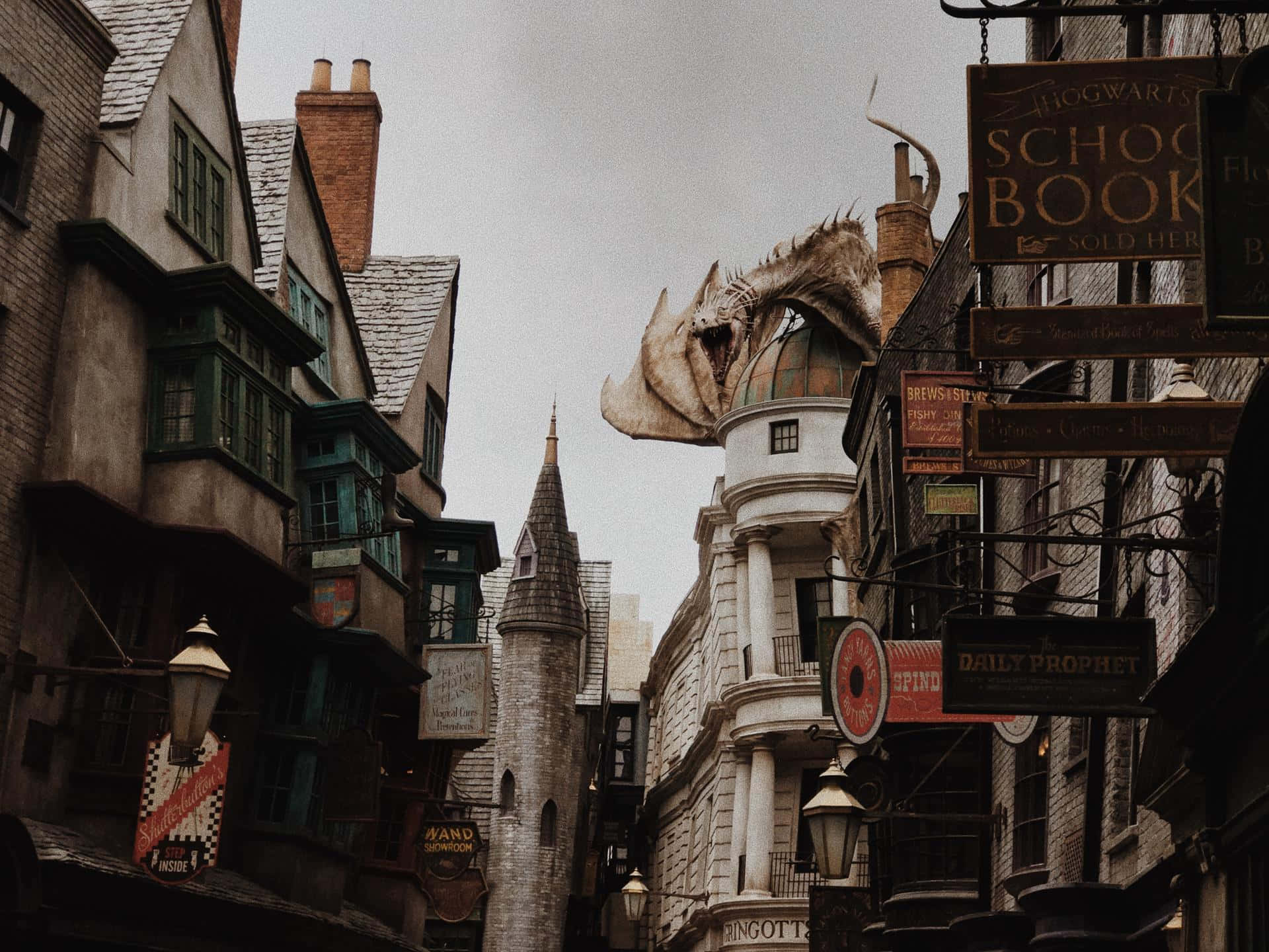 Hogsmeade 桌布 壁紙 — 斜角巷一條狹窄的鵝卵石街道上，有一條龍棲息在一棟建築物頂部，上方懸掛著霍格華茲學校書店的招牌。