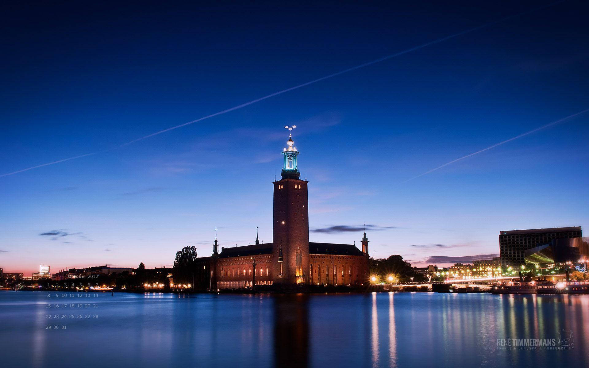 Sweden 桌布 壁紙 — 斯德哥爾摩大教堂在暮色中亮起燈光，城市燈光倒映在平靜的水面上。