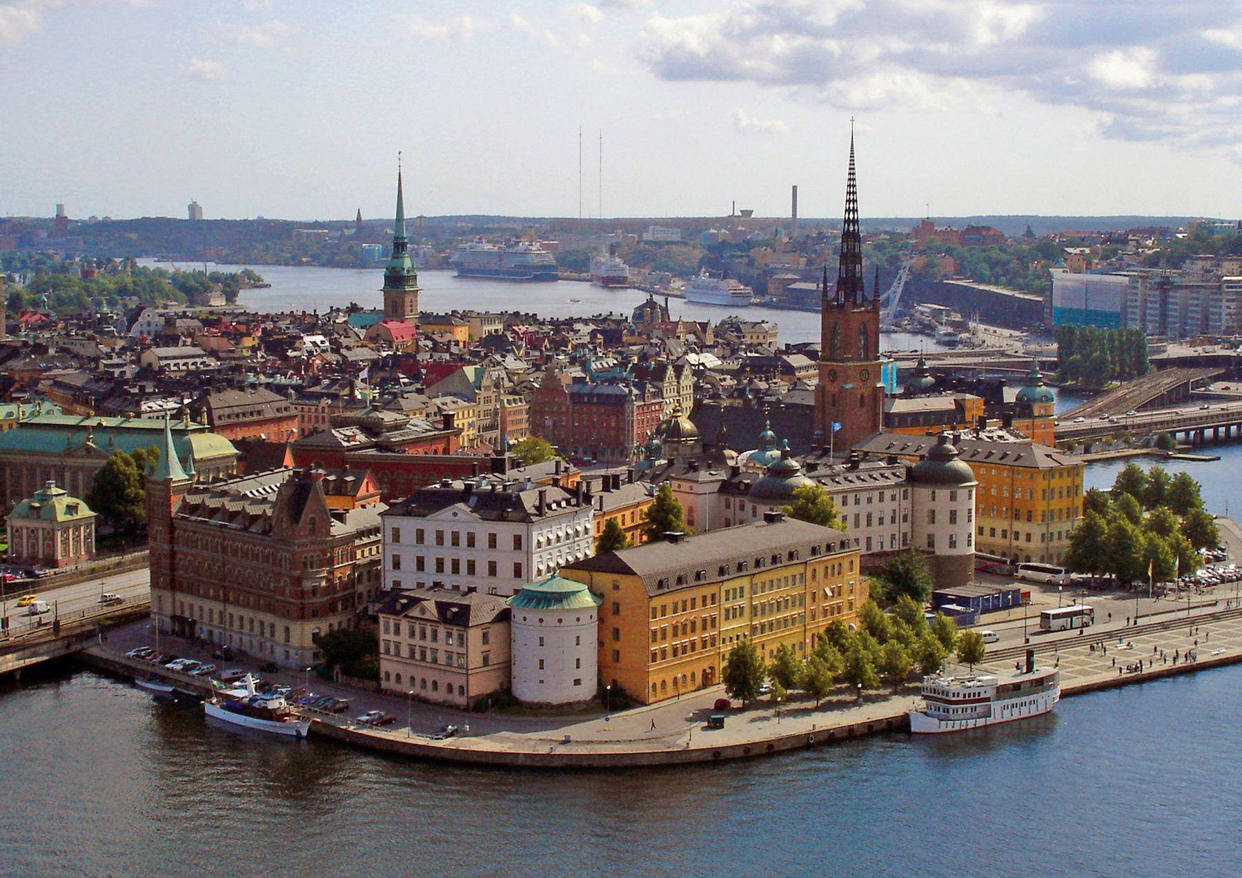 Sweden 桌布 壁紙 — 斯德哥爾摩歷史區的鳥瞰圖，色彩繽紛的建築、尖塔和船隻沿著蜿蜒的水道，在部分多雲的天空下。
