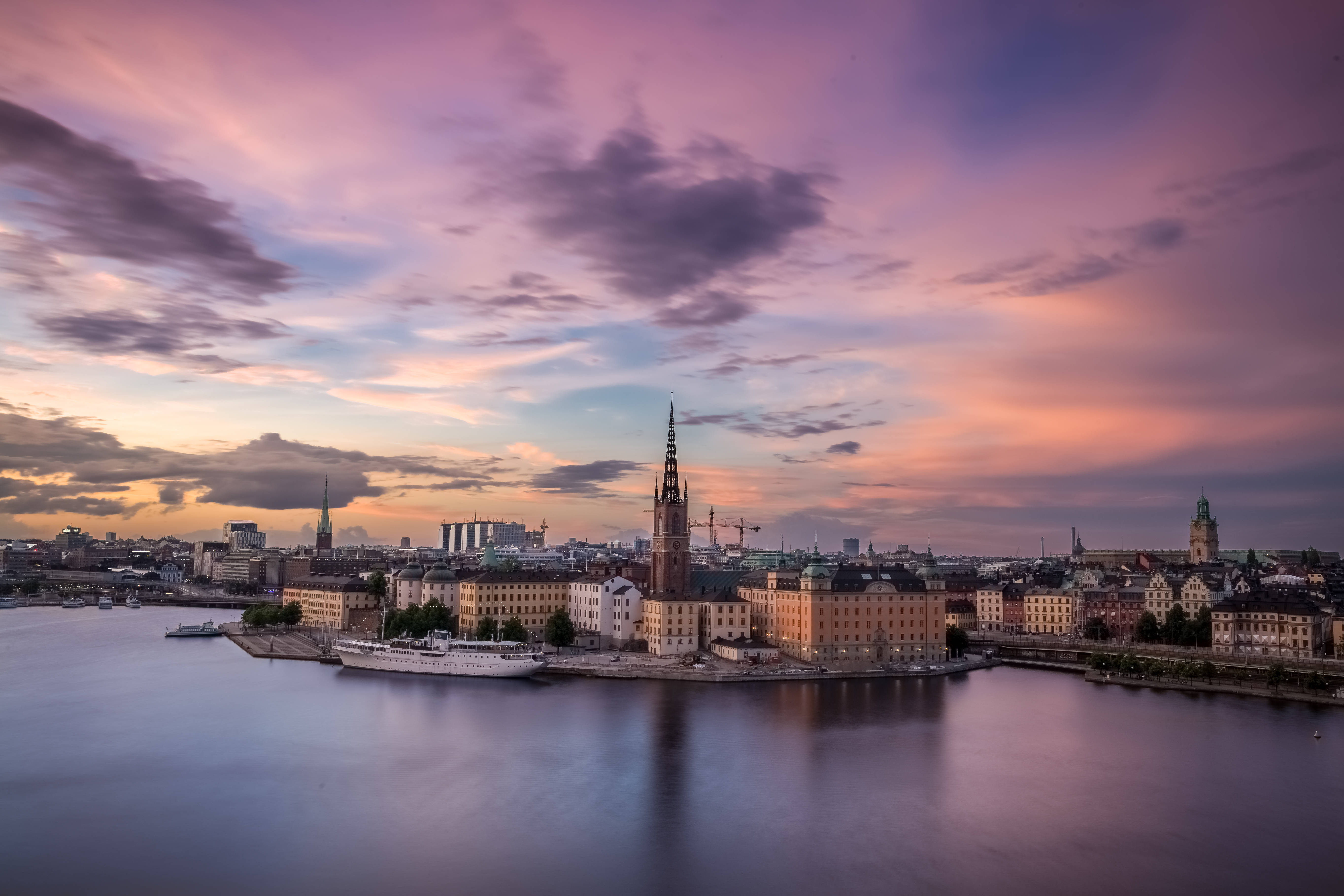 Sweden 桌布 壁紙 — 斯德哥爾摩歷史悠久的海濱上空，壯麗的日落，粉彩粉紅和橙色雲彩映照在平靜的水面上。