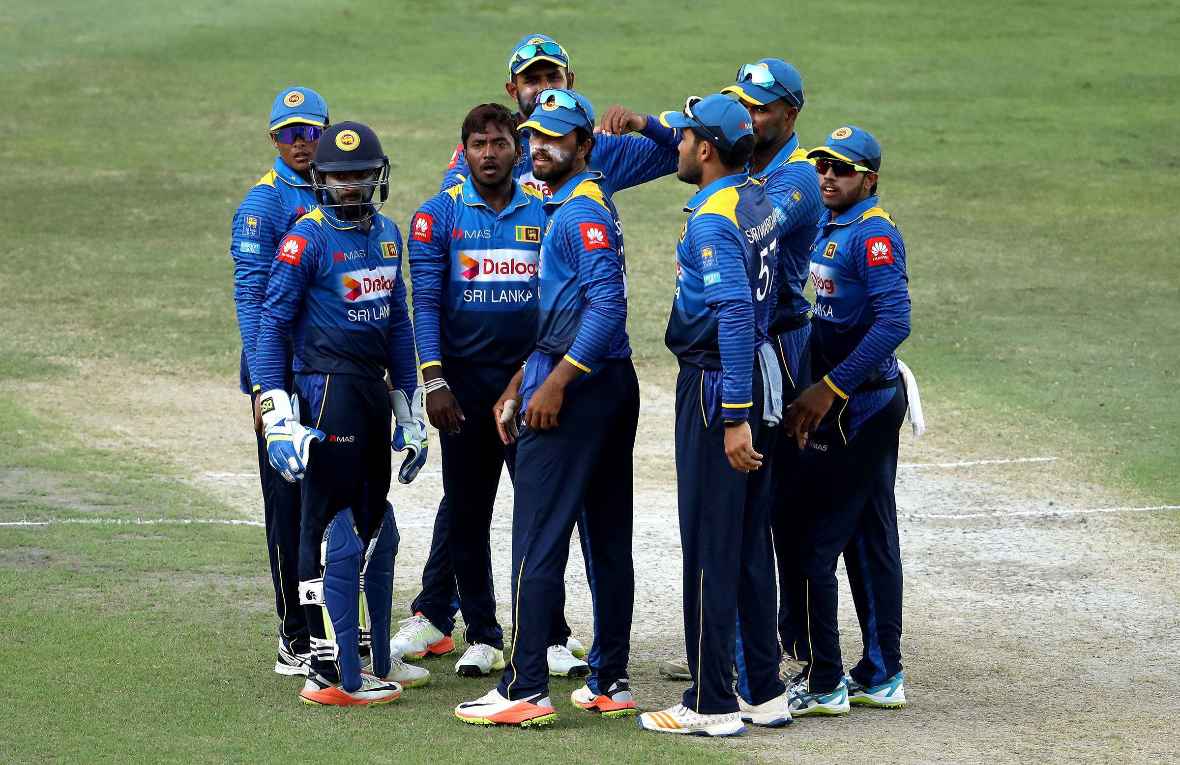 Sri Lanka Cricket 桌布 壁紙 — 斯里蘭卡板球隊在日間比賽中聚集在綠色場地上，穿著帶有贊助商標誌的藍色制服。