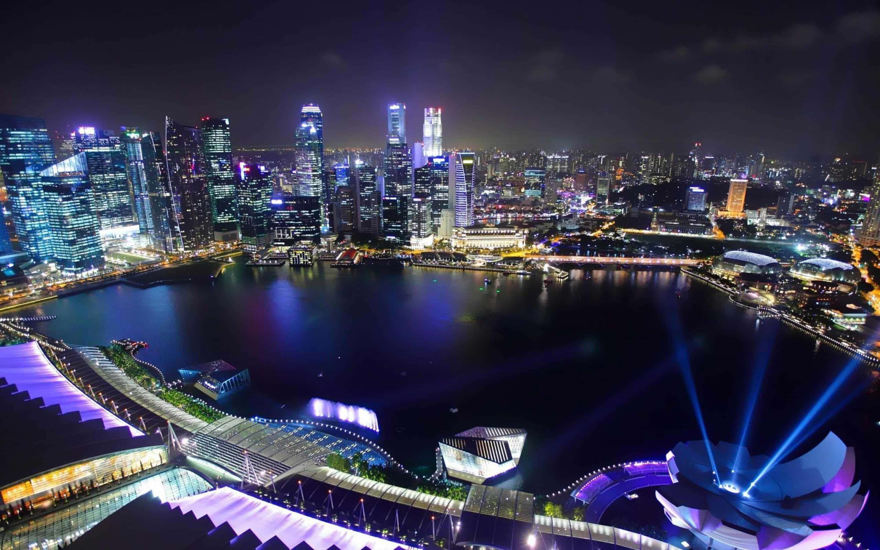 城市風景 桌布 壁紙 — 新加坡令人眼花繚亂的夜景，閃閃發光的摩天大樓倒映在濱海灣，充滿活力的藍色雷射光束照亮了海濱。