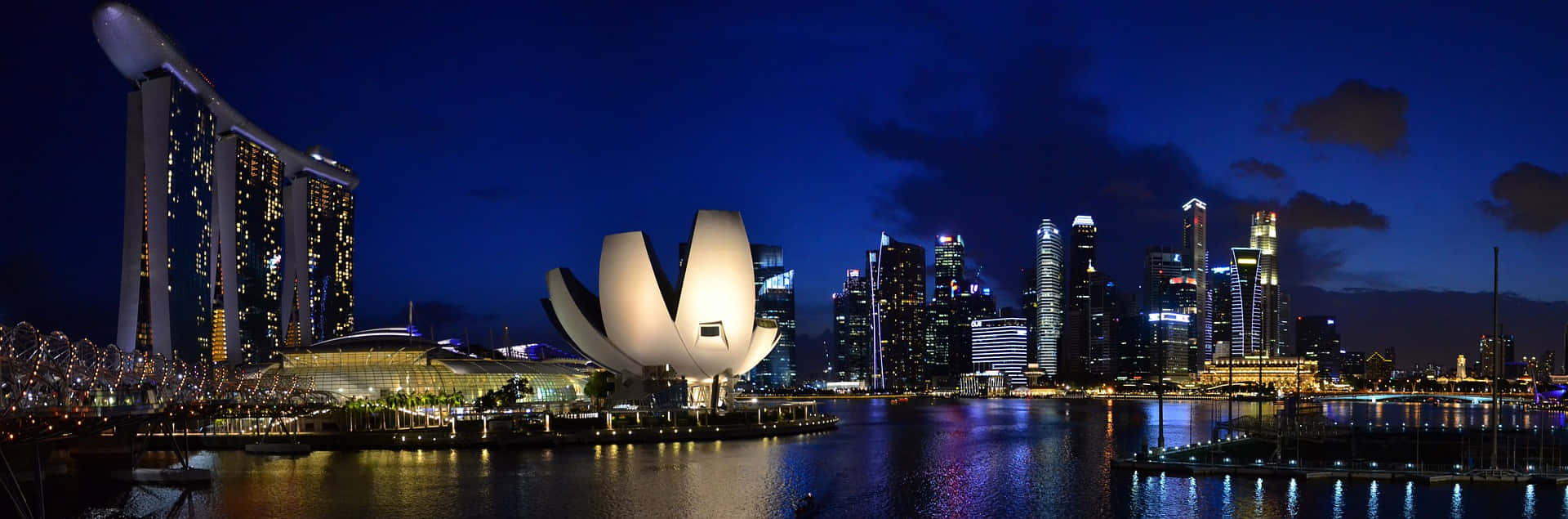 Panoramic 桌布 壁紙 — 新加坡天際線的 panoramic 夜景，濱海灣金沙和藝術科學博物館在深藍色天空和反射水面上閃耀。