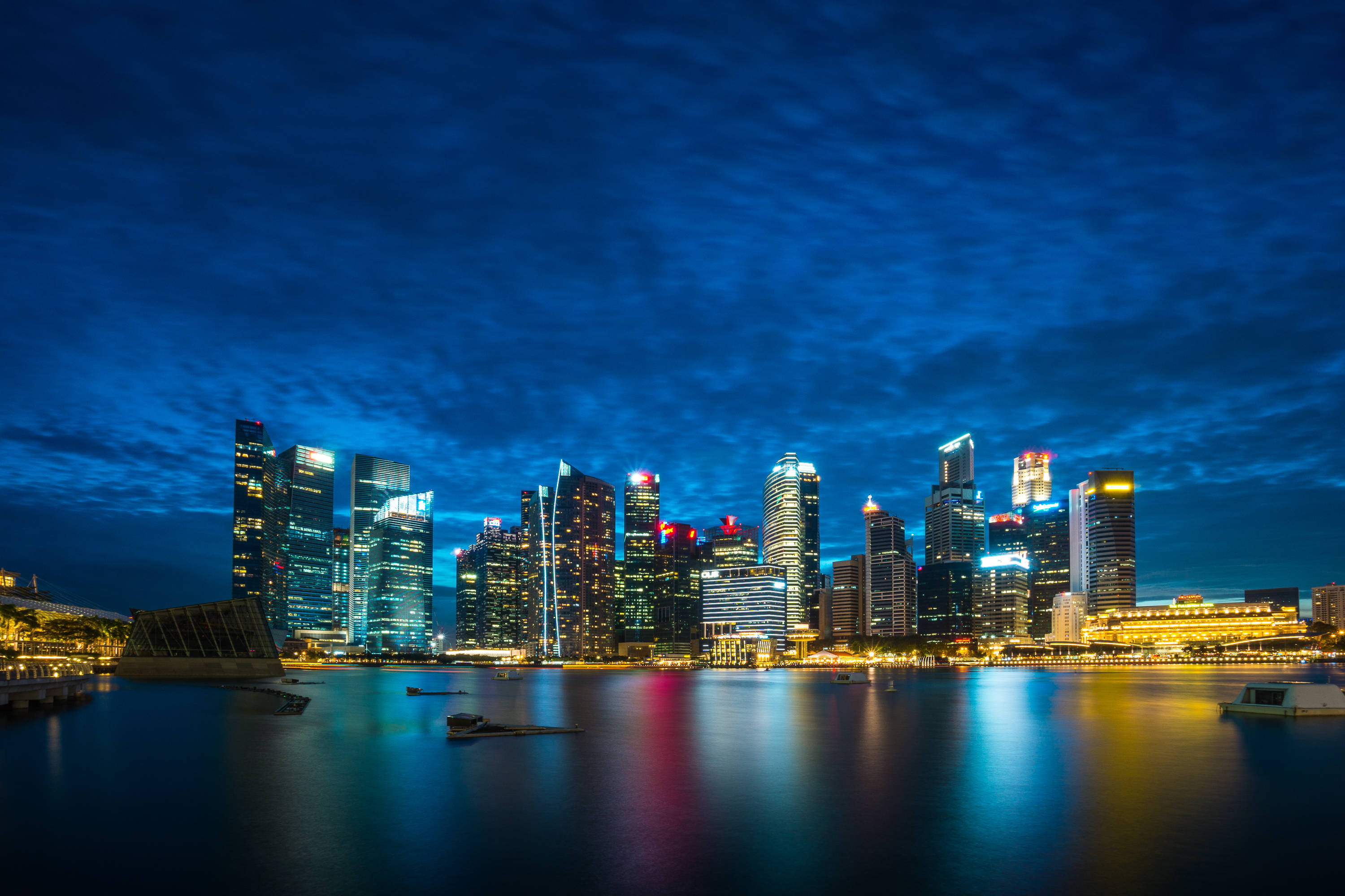 Singapore 桌布 壁紙 — 新加坡天際線的壯麗夜景，在深藍色天空下，燈火通明的摩天大樓倒映在平靜的水面上。