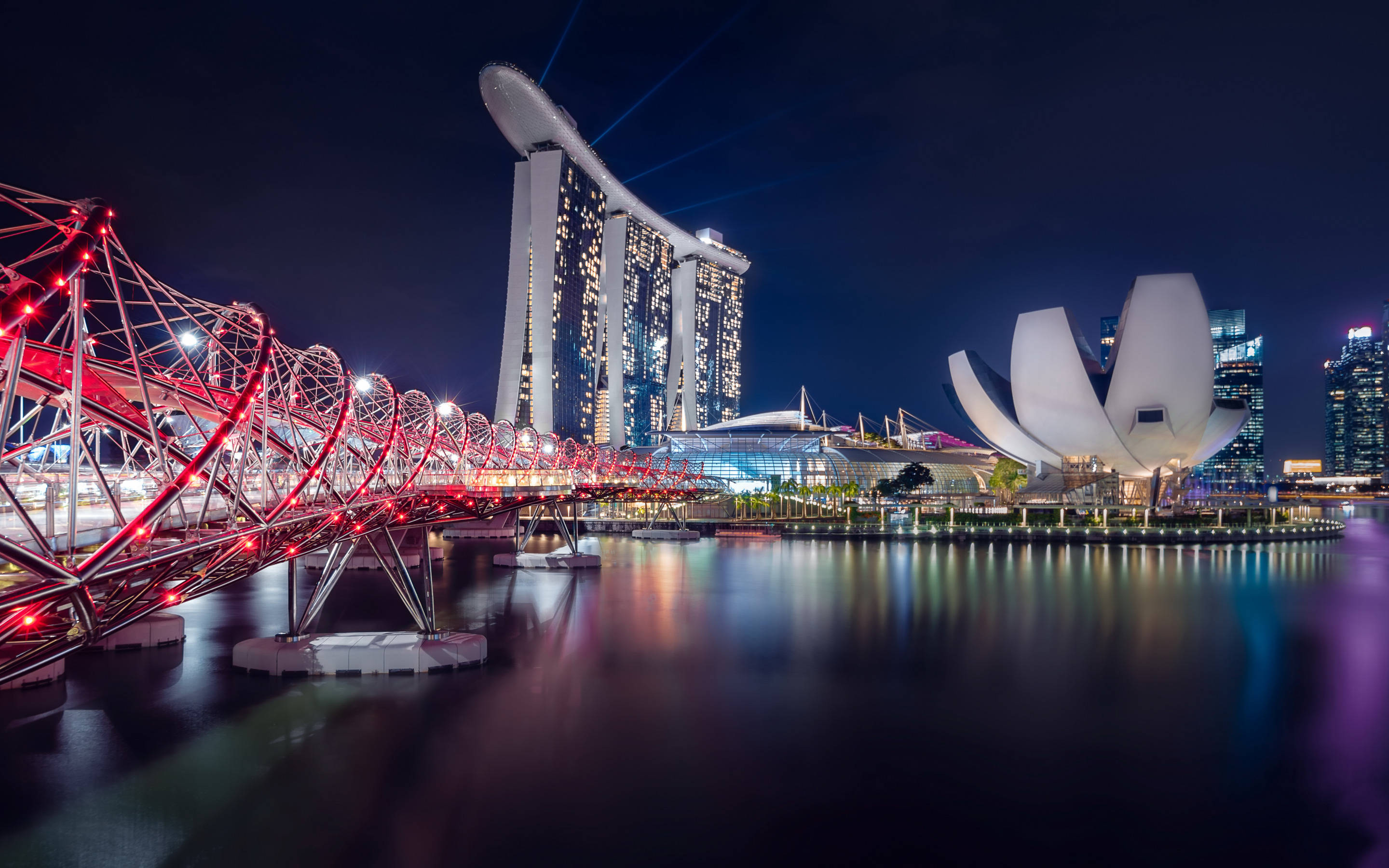 美麗 桌布 壁紙 — 新加坡天際線的璀璨夜景，以標誌性的濱海灣金沙和藝術科學博物館為特色，平靜的水面上有一座發光的紅色橋樑。