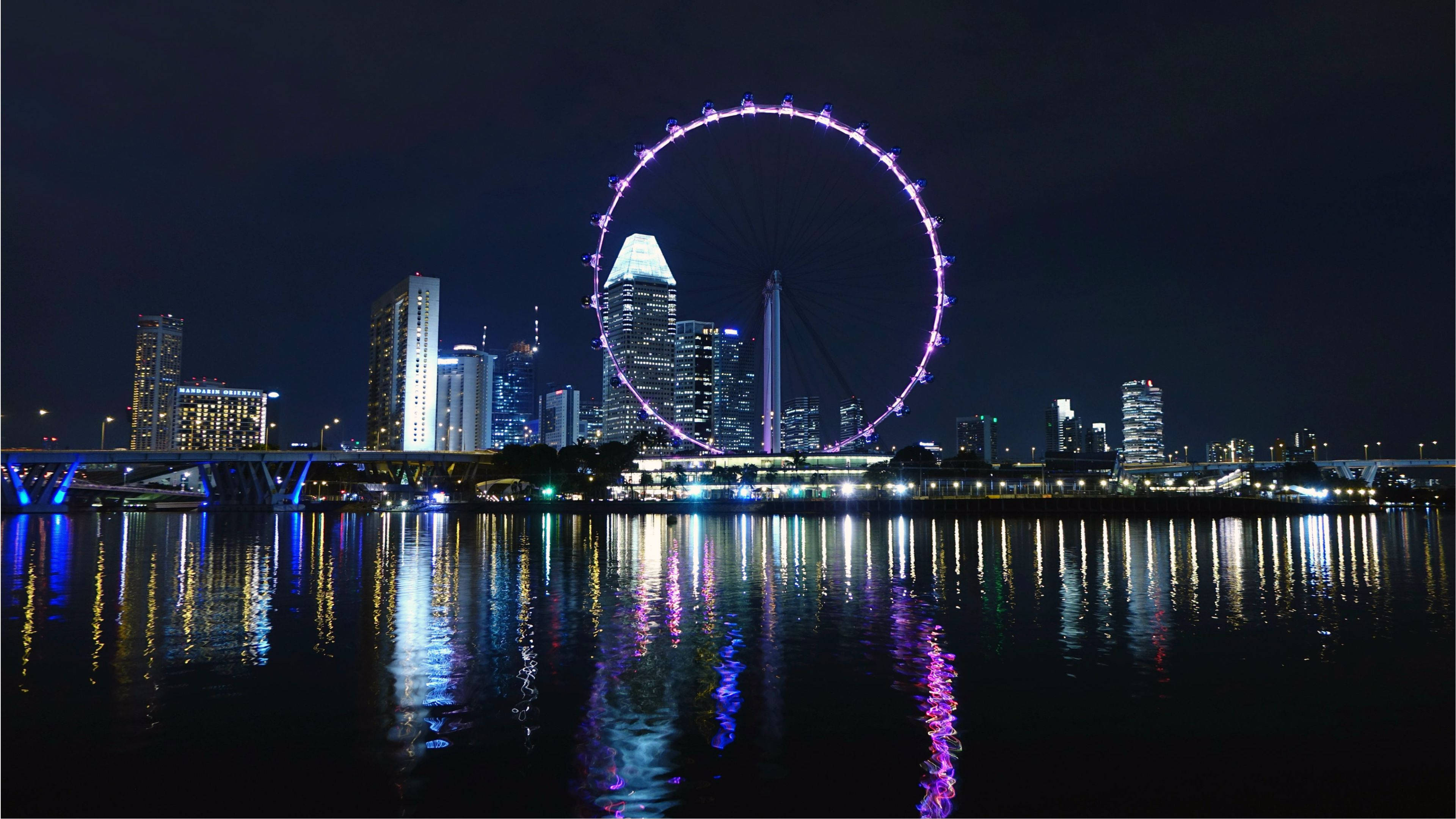 Singapore 桌布 壁紙 — 新加坡天際線的璀璨夜景，標誌性的新加坡摩天輪在反射水道上發出紫色光芒。