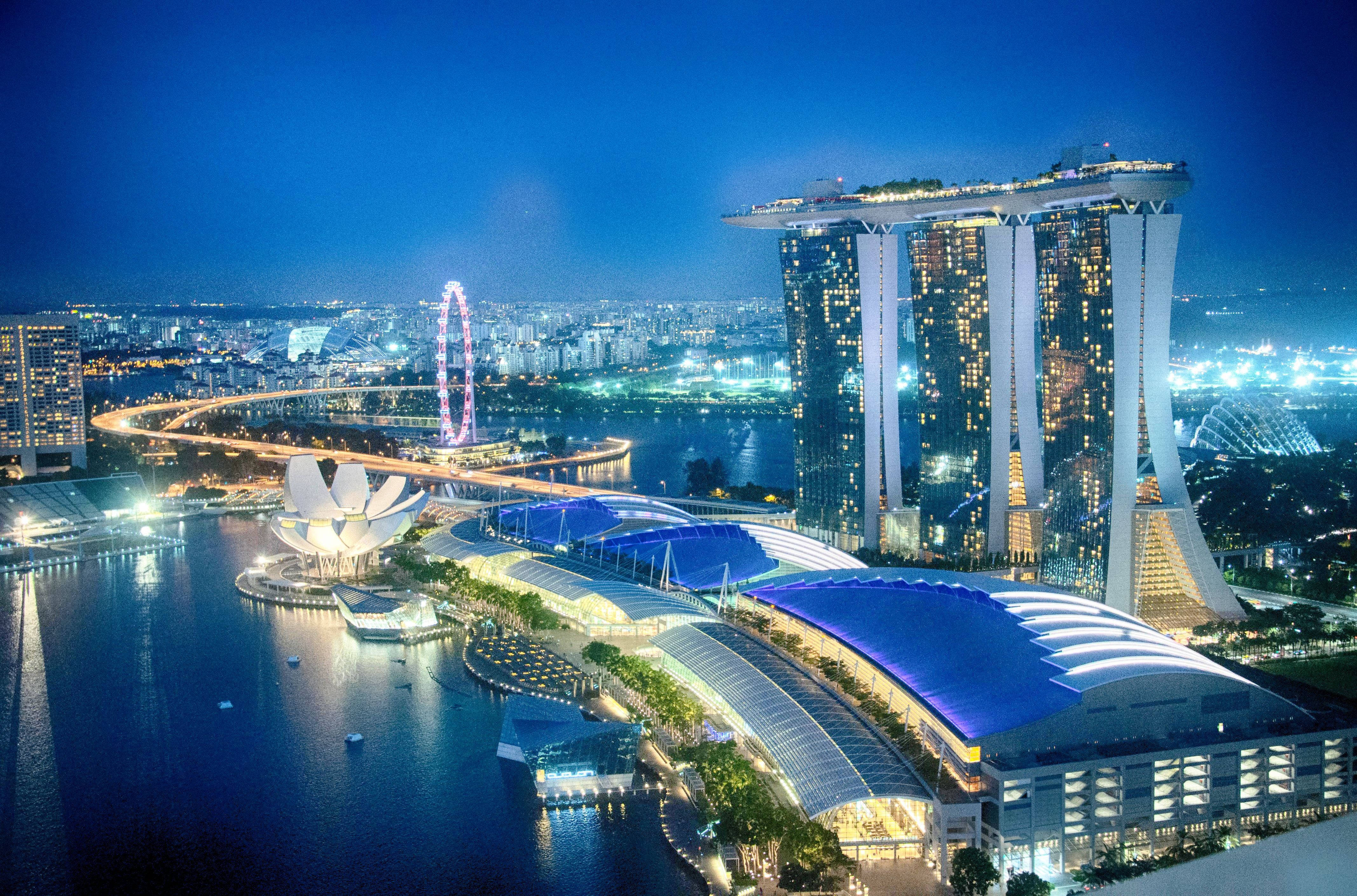 夜晚 桌布 壁紙 — 新加坡天際線的迷人夜景，包括濱海灣金沙酒店和新加坡摩天觀景輪，背景是深藍色的天空。