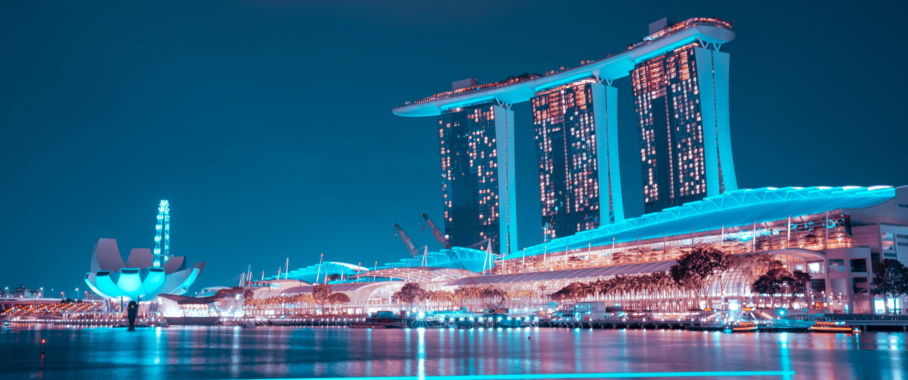 Singapore 桌布 壁紙 — 新加坡濱海灣的迷人夜景，標誌性的濱海灣金沙酒店和藝術科學博物館在平靜的水面上閃爍著藍色和溫暖的燈光。