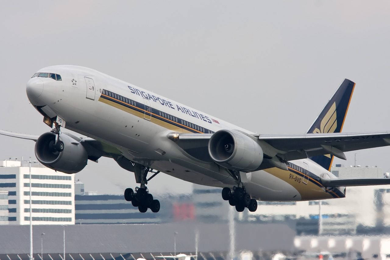 飛機 桌布 壁紙 — 新加坡航空的波音777在起飛時起落架伸出，背景是朦朧的城市景觀。