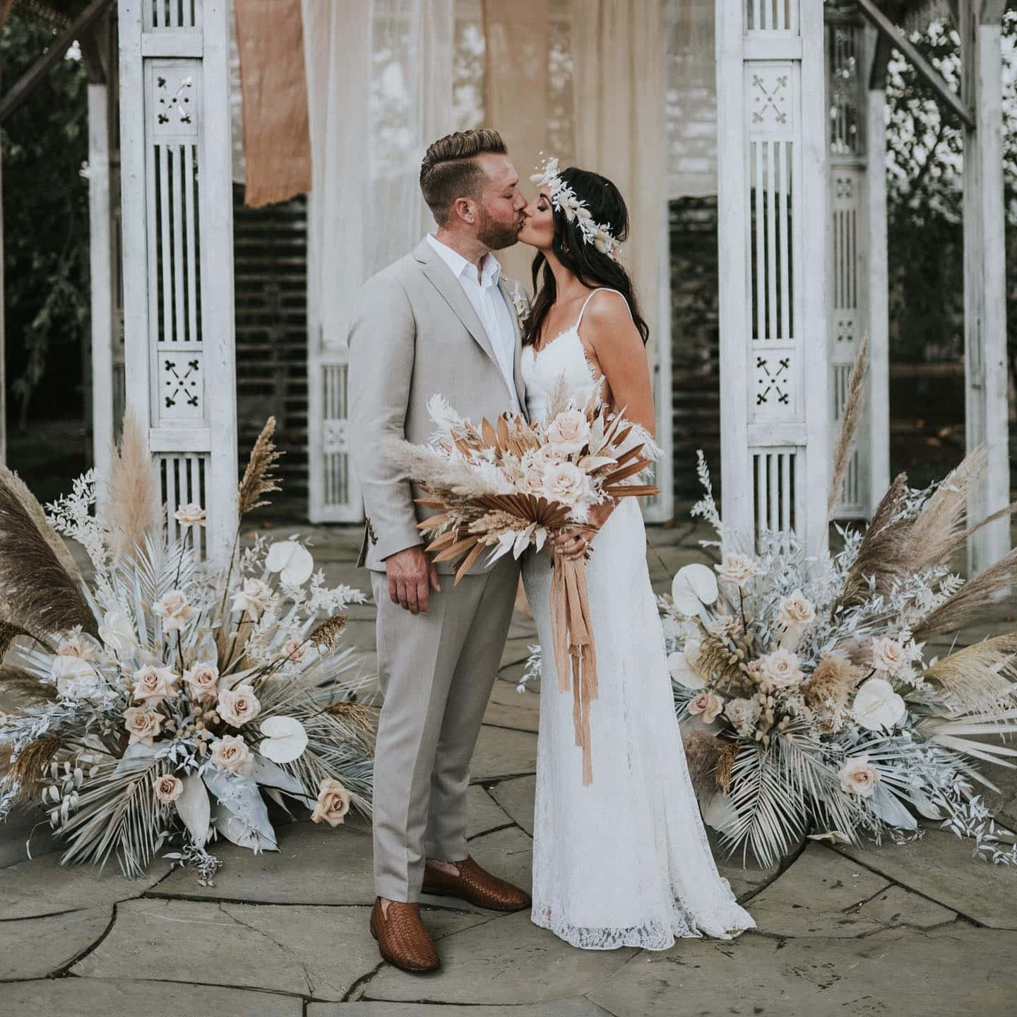 Groom And Bride 桌布 壁紙 — 新娘和新郎在一個裝飾著乾燥蒲葦和柔軟蜜桃玫瑰的白色木製涼亭下接吻。