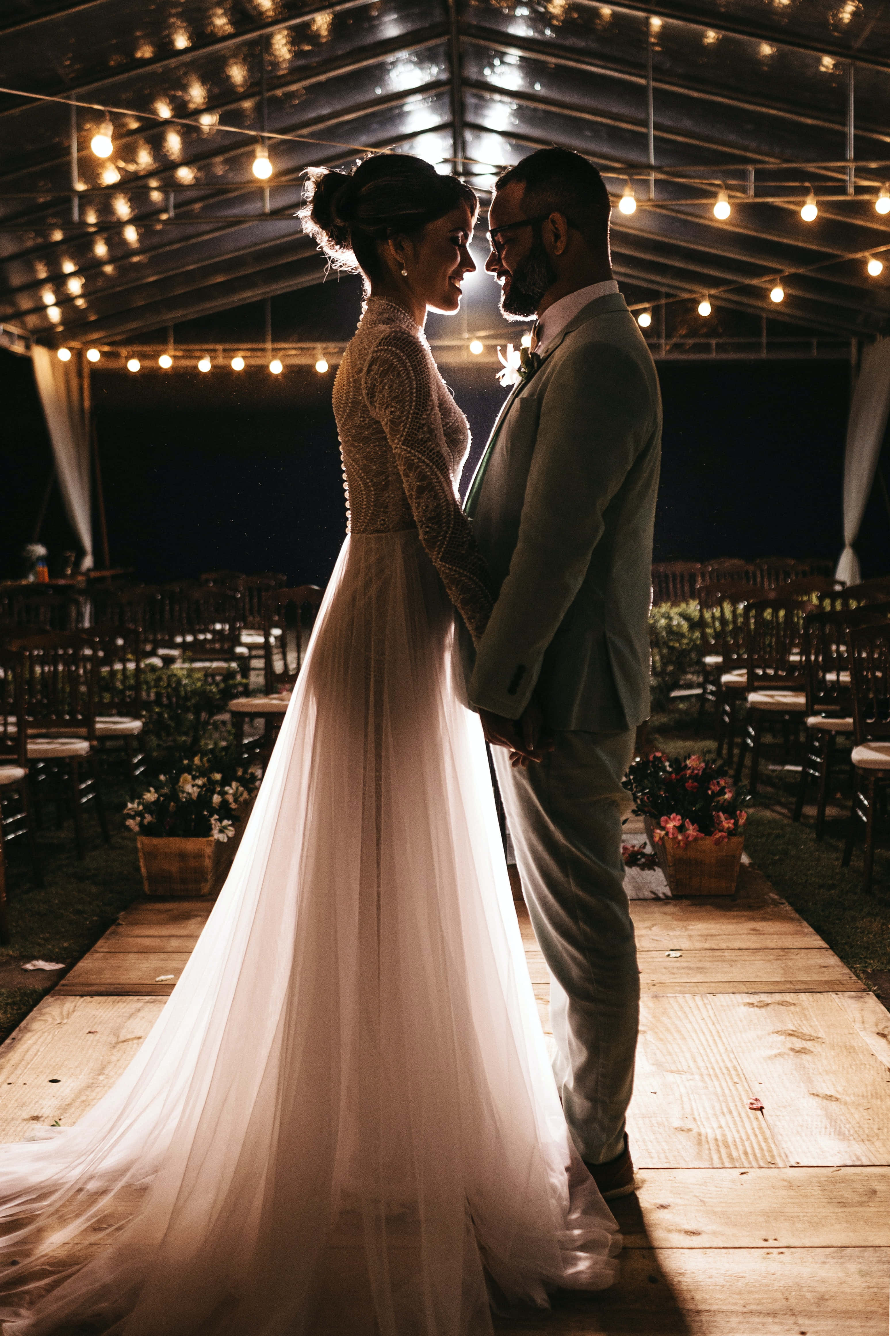 Groom And Bride 桌布 壁紙 — 新娘和新郎在夜間戶外婚禮上，在串燈下面對面站立。