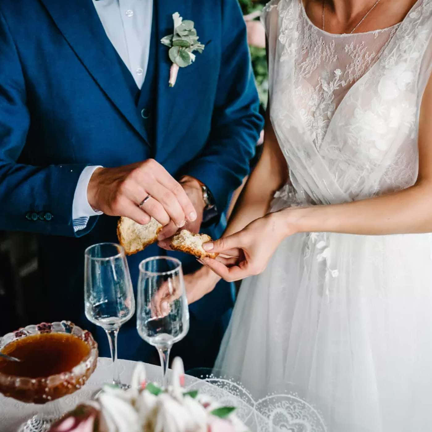 Groom And Bride 桌布 壁紙 — 新娘和新郎在婚禮桌上分享掰麵包的時刻，配有酒杯和裝飾碗。