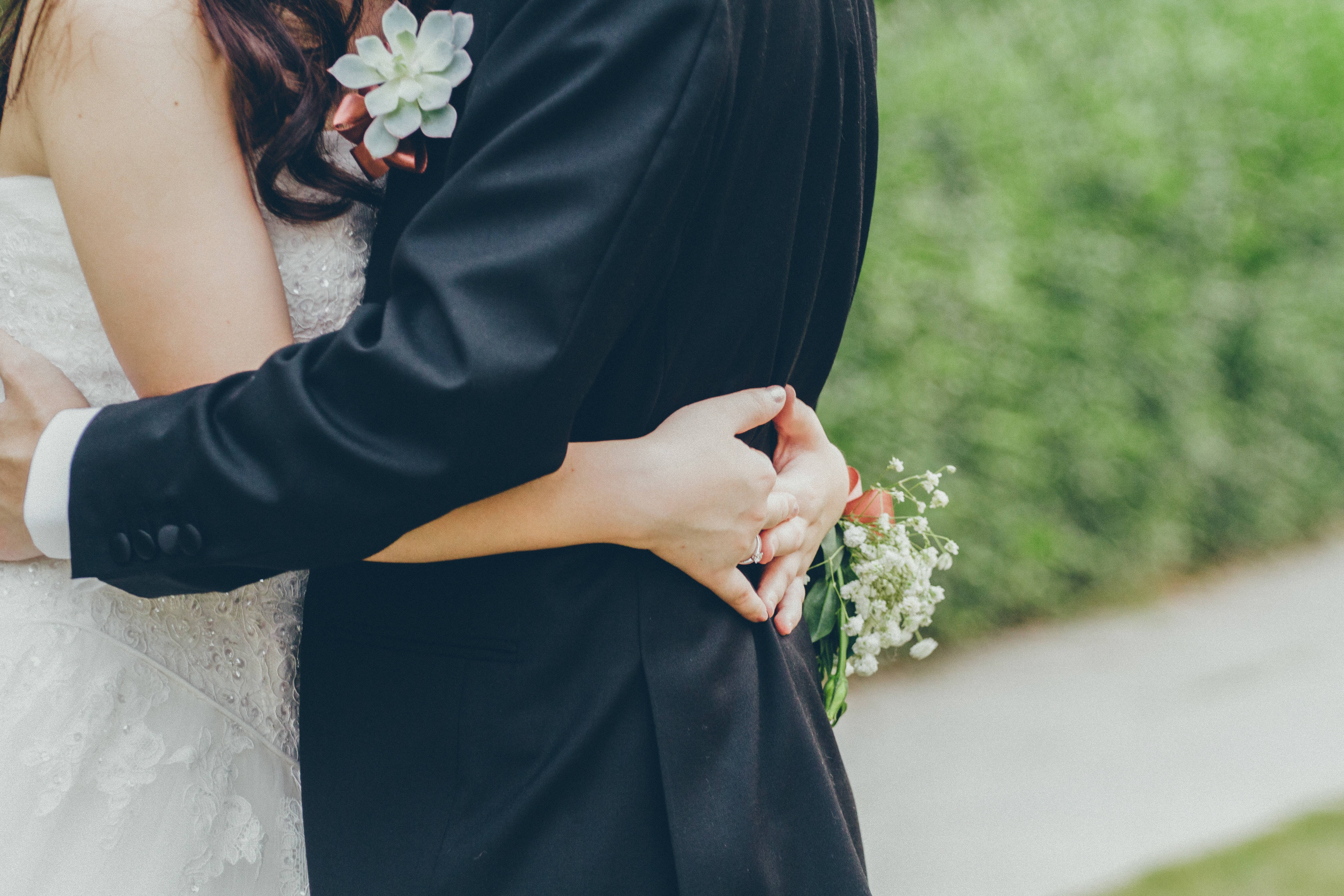 Romantic Love 桌布 壁紙 — 新娘和新郎在戶外溫柔擁抱，婚禮鮮花與柔和模糊的綠色背景相映襯。
