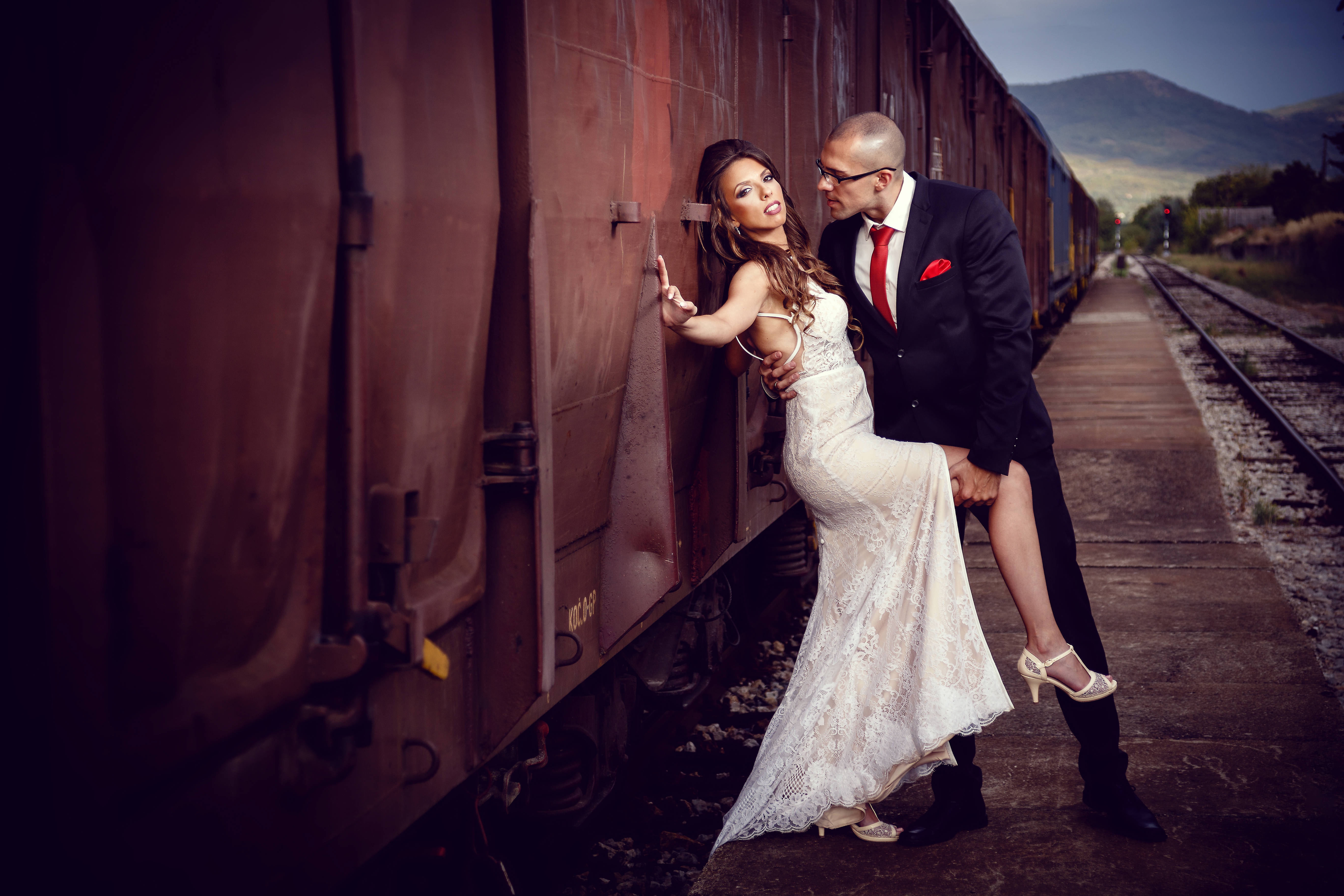 Groom 桌布 壁紙 — 新娘和新郎在火車月台上，背景有山巒，親密地在一輛生鏽的火車車廂旁擺姿勢。