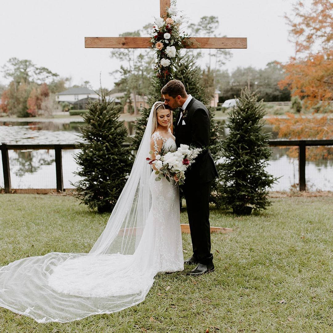 Wedding 桌布 壁紙 — 新娘和新郎在秋樹環繞的池塘旁的花卉十字拱門下擁抱。