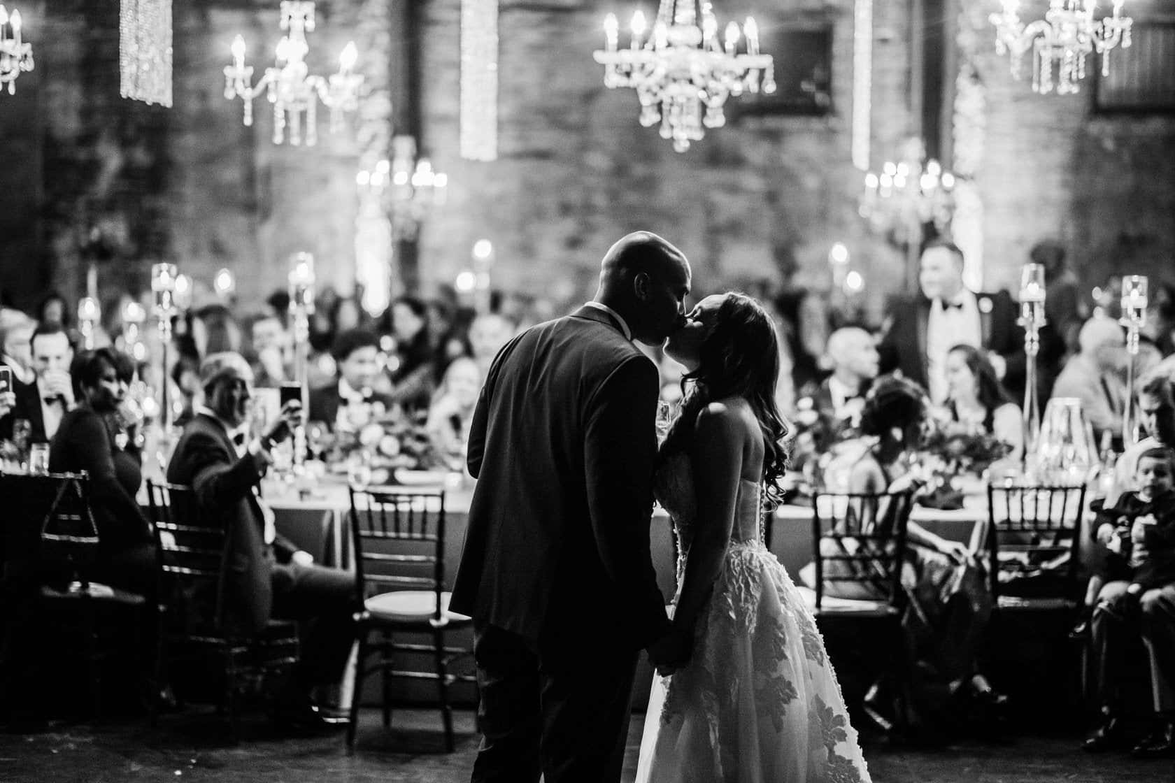 Black And White Wedding 桌布 壁紙 — 新娘和新郎在閃爍的水晶燈下，在婚宴上熱情接吻，賓客們在旁觀看。