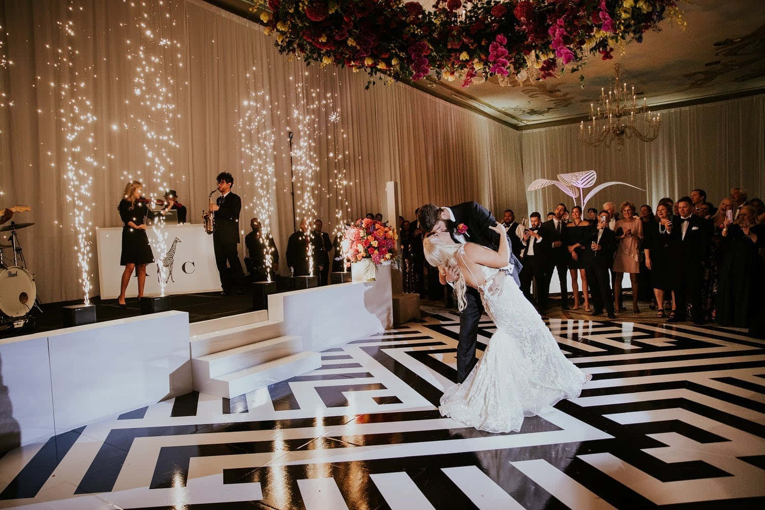 Black And White Wedding 桌布 壁紙 — 新娘和新郎在黑白幾何圖案的舞池上熱情接吻，賓客觀看，煙火從窗簾背景中如瀑布般落下。