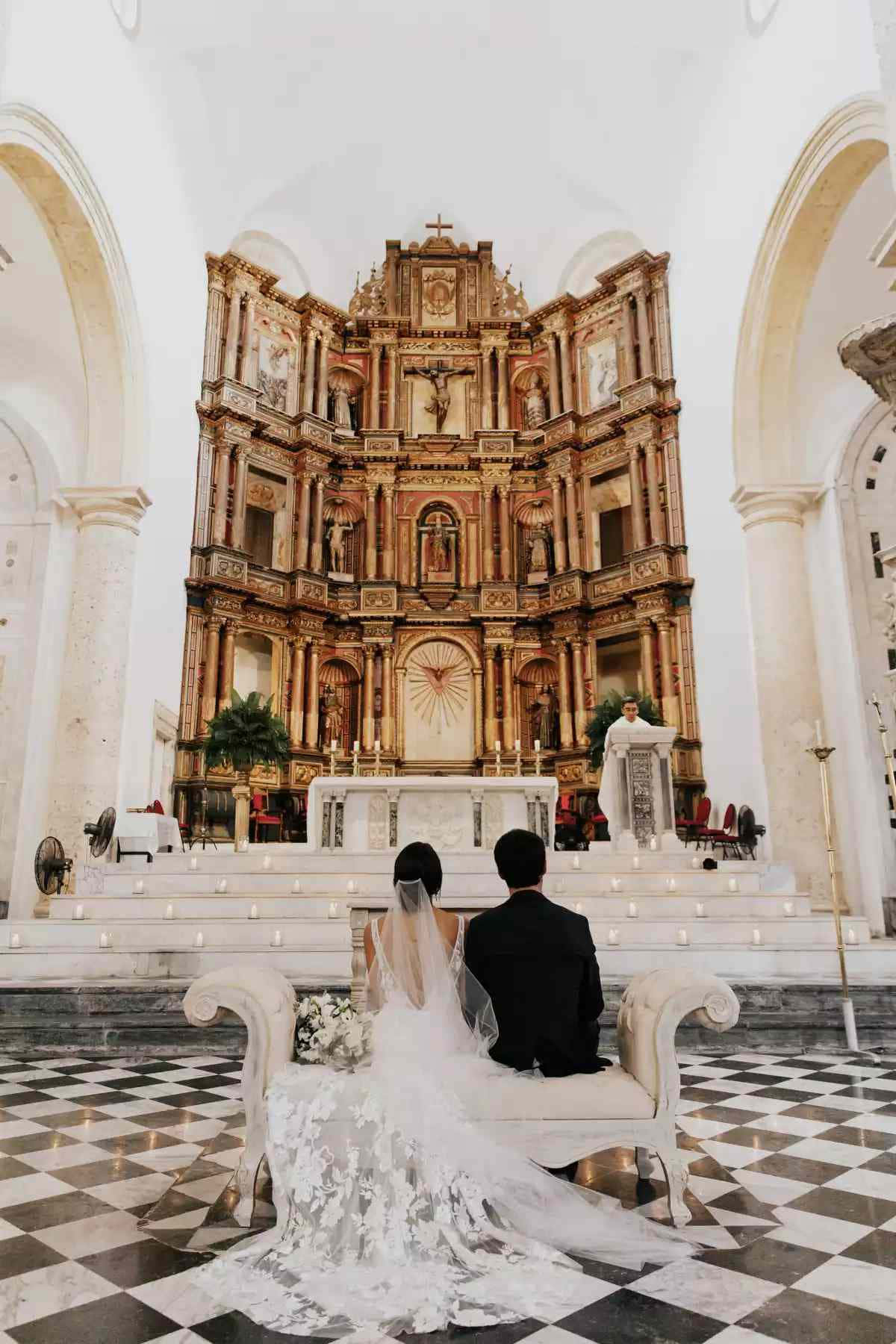 Wedding Aesthetic 桌布 壁紙 — 新娘和新郎坐在白色長椅上，面向大教堂內裝飾華麗的金色祭壇，地板是棋盤格圖案。