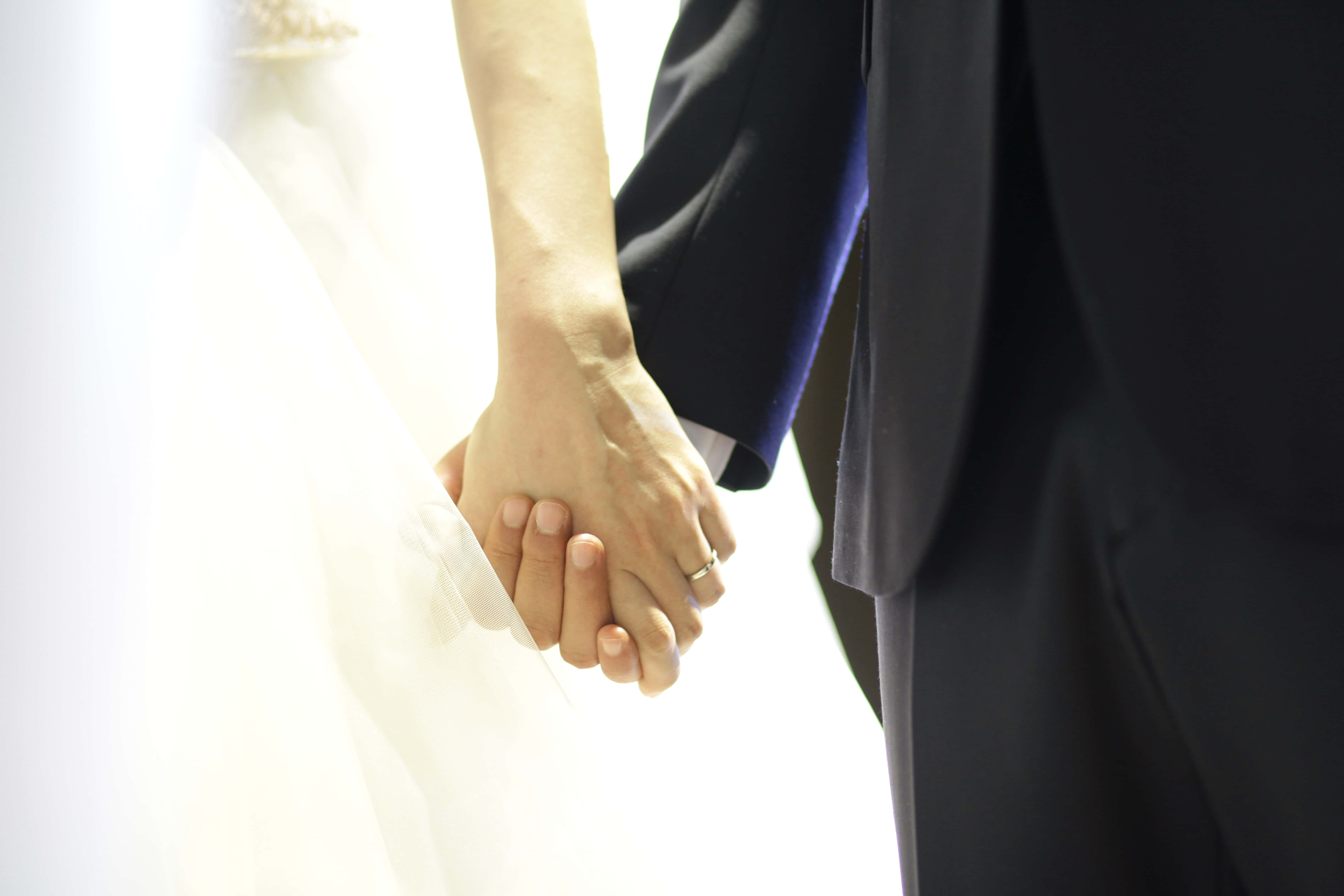 Couple Holding Hand 桌布 壁紙 — 新娘和新郎的手緊握在一起的特寫，結婚戒指在柔和背光中閃耀。