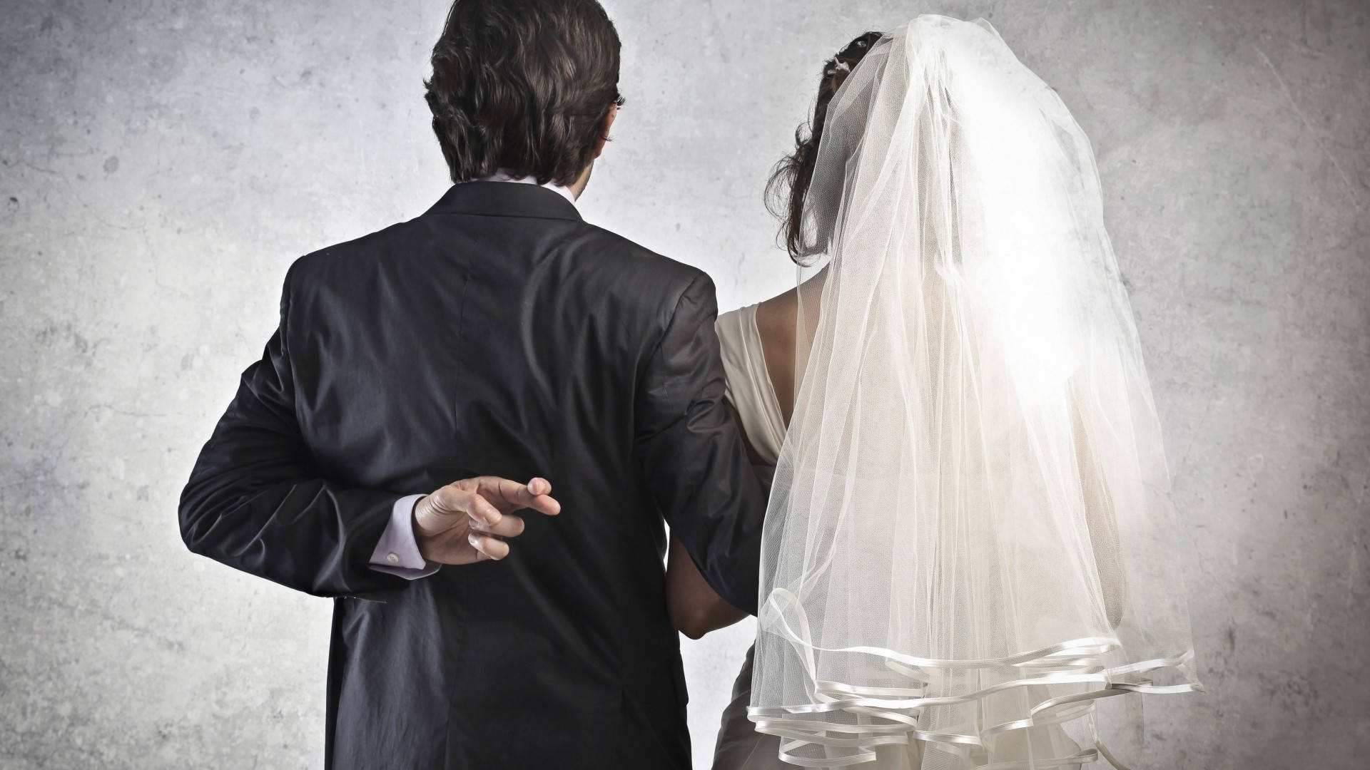 Wedding 桌布 壁紙 — 新娘和新郎背對背站立，身穿婚紗禮服，背景是紋理灰色牆壁，雙手輕柔觸碰。