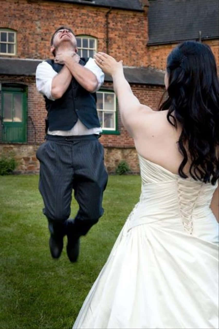Funny Wedding 桌布 壁紙 — 新娘在磚砌建築前的歡樂花園婚禮時刻將新郎拋向空中。