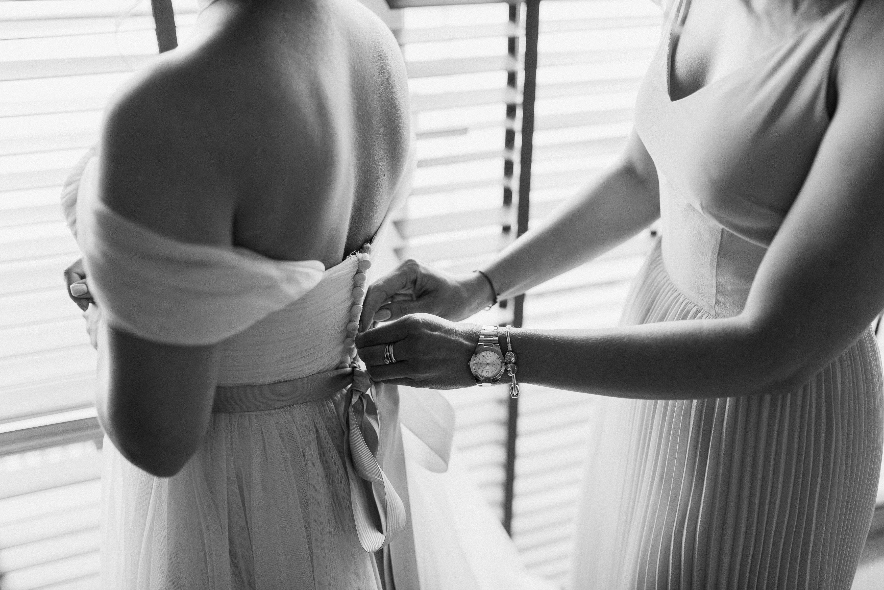 Bridal 桌布 壁紙 — 新娘的背影，伴娘在窗邊百葉窗旁為她繫上婚紗絲帶。