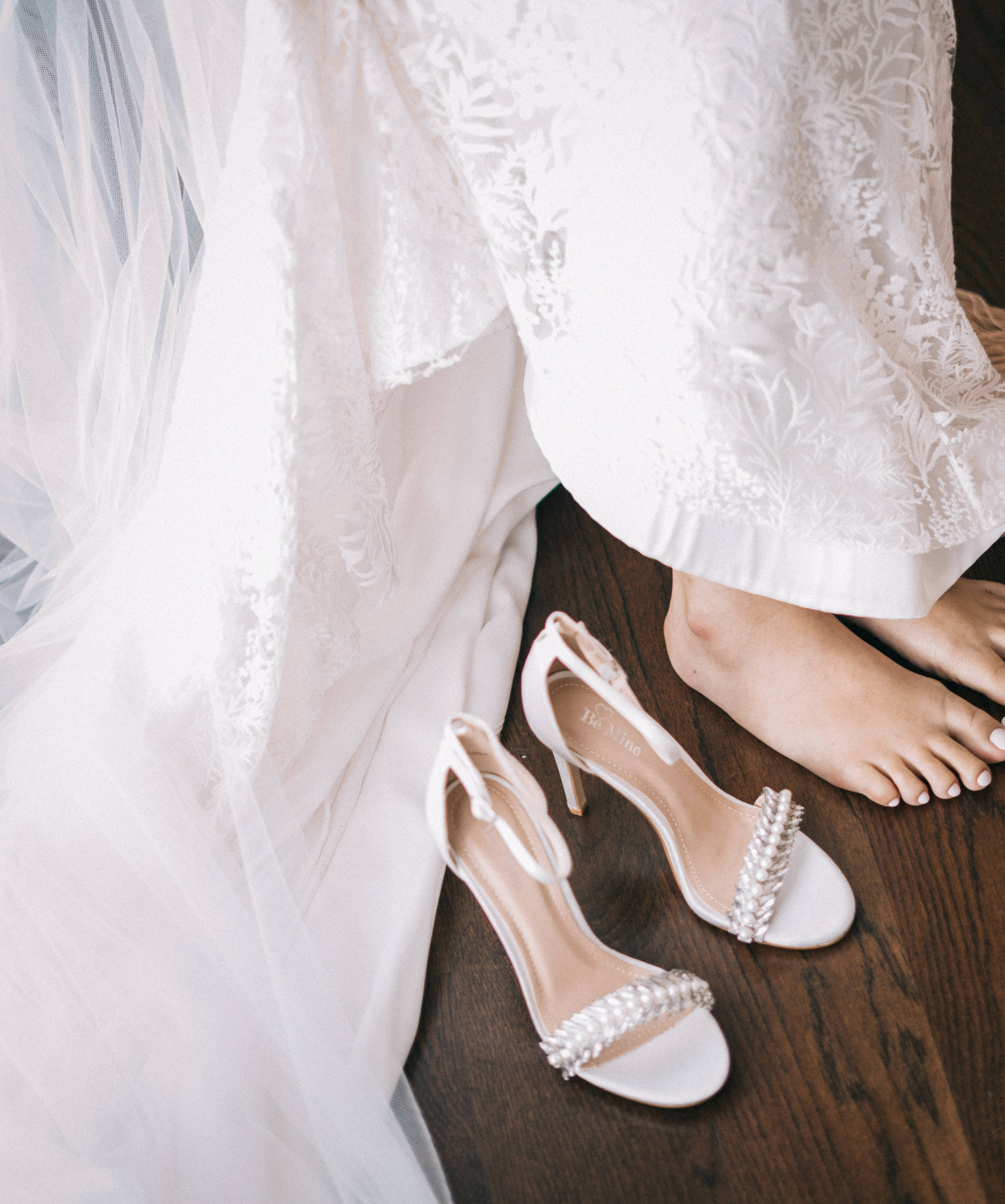 Bridal 桌布 壁紙 — 新娘的赤腳放在木地板上流暢的蕾絲婚紗下的白色珠飾高跟鞋旁邊。