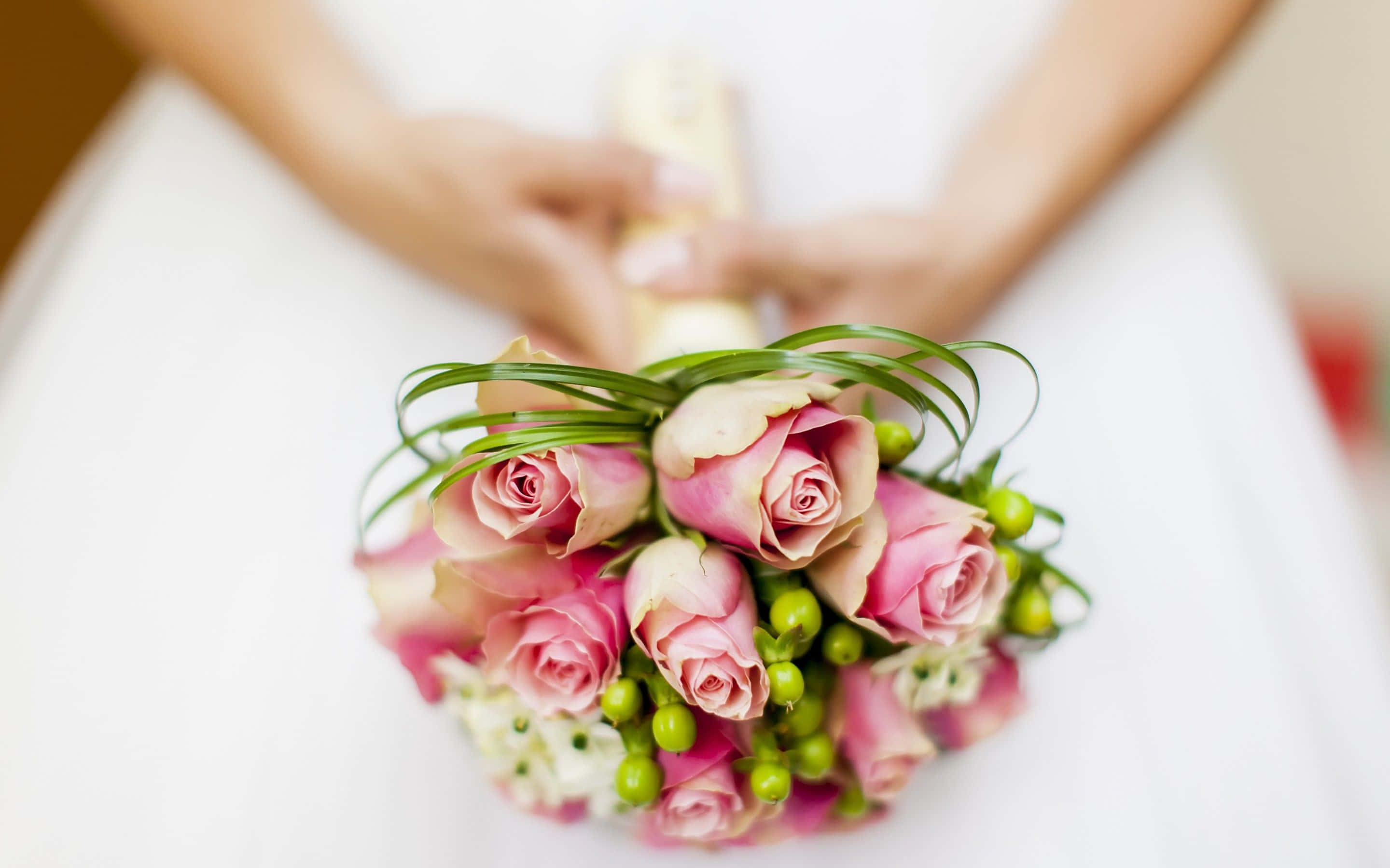 Wedding Flowers 桌布 壁紙 — 新娘雙手捧著精緻的粉紅玫瑰和綠色漿果花束，襯托柔軟白色婚紗的特寫。