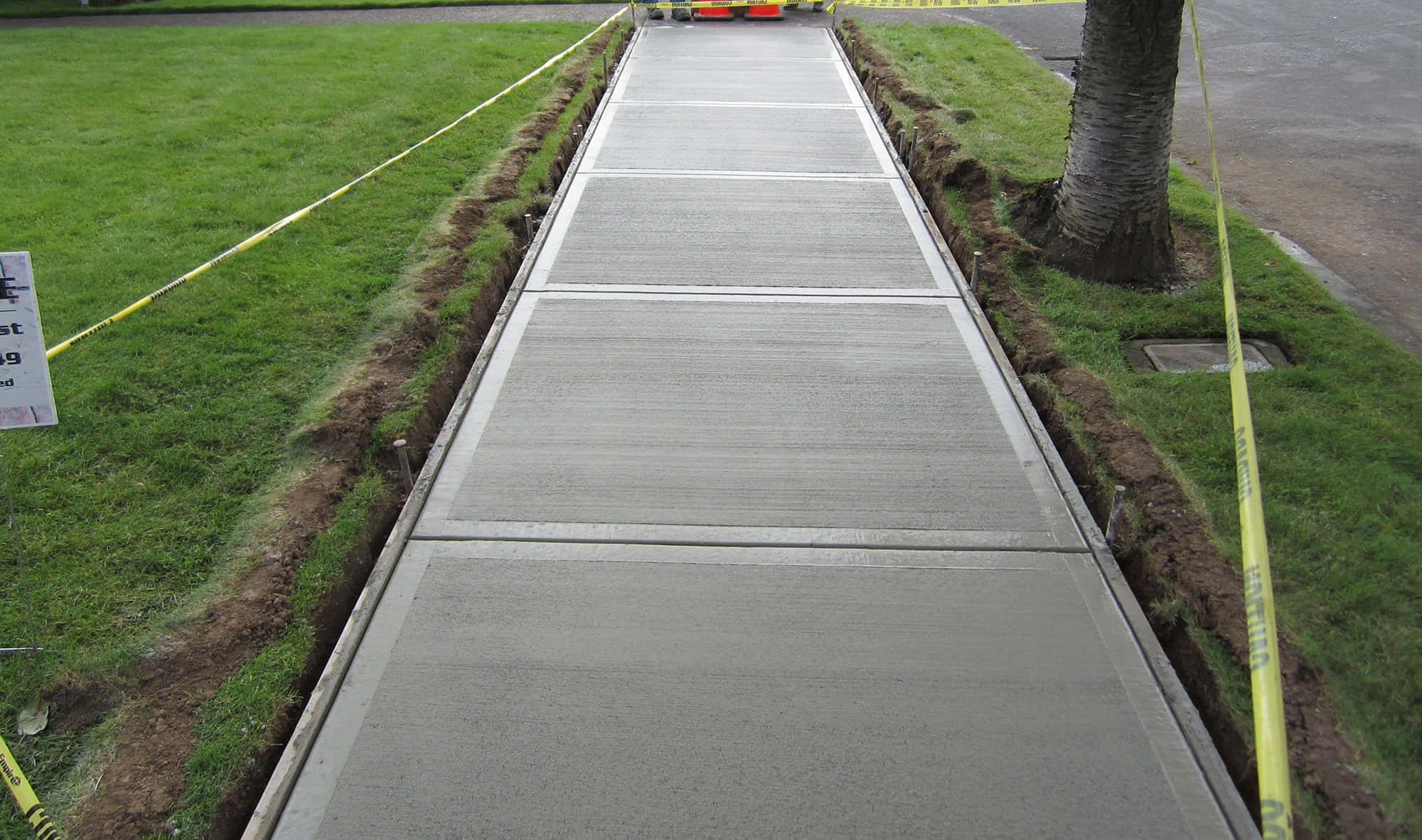 Sidewalk 桌布 壁紙 — 新澆築的混凝土人行道筆直向前延伸，兩旁是綠色草地和黃色警示膠帶。