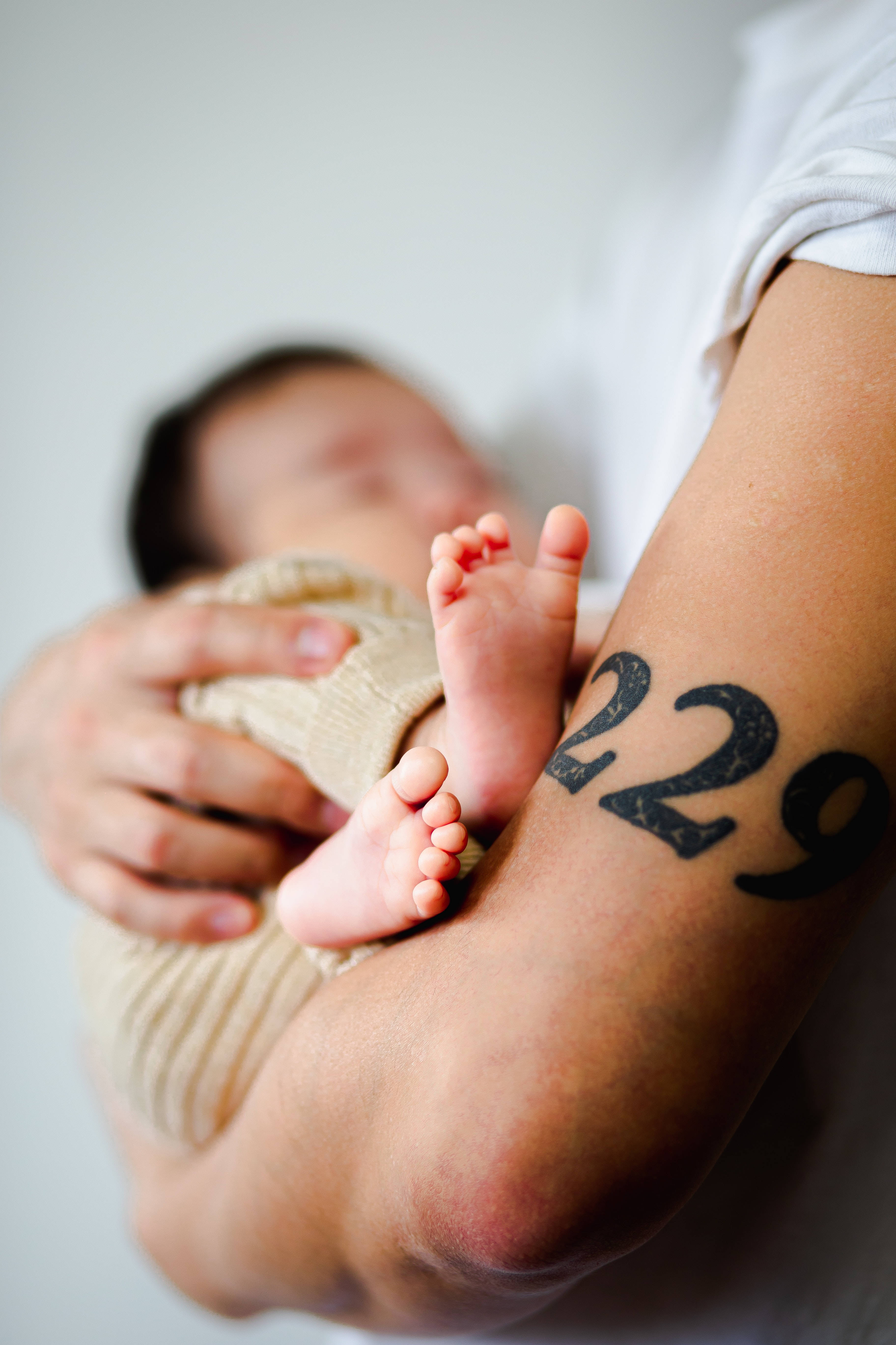 Newborn 桌布 壁紙 — 新生兒小腳丫放在成人手臂上的特寫，可見一個粗體的229刺青。