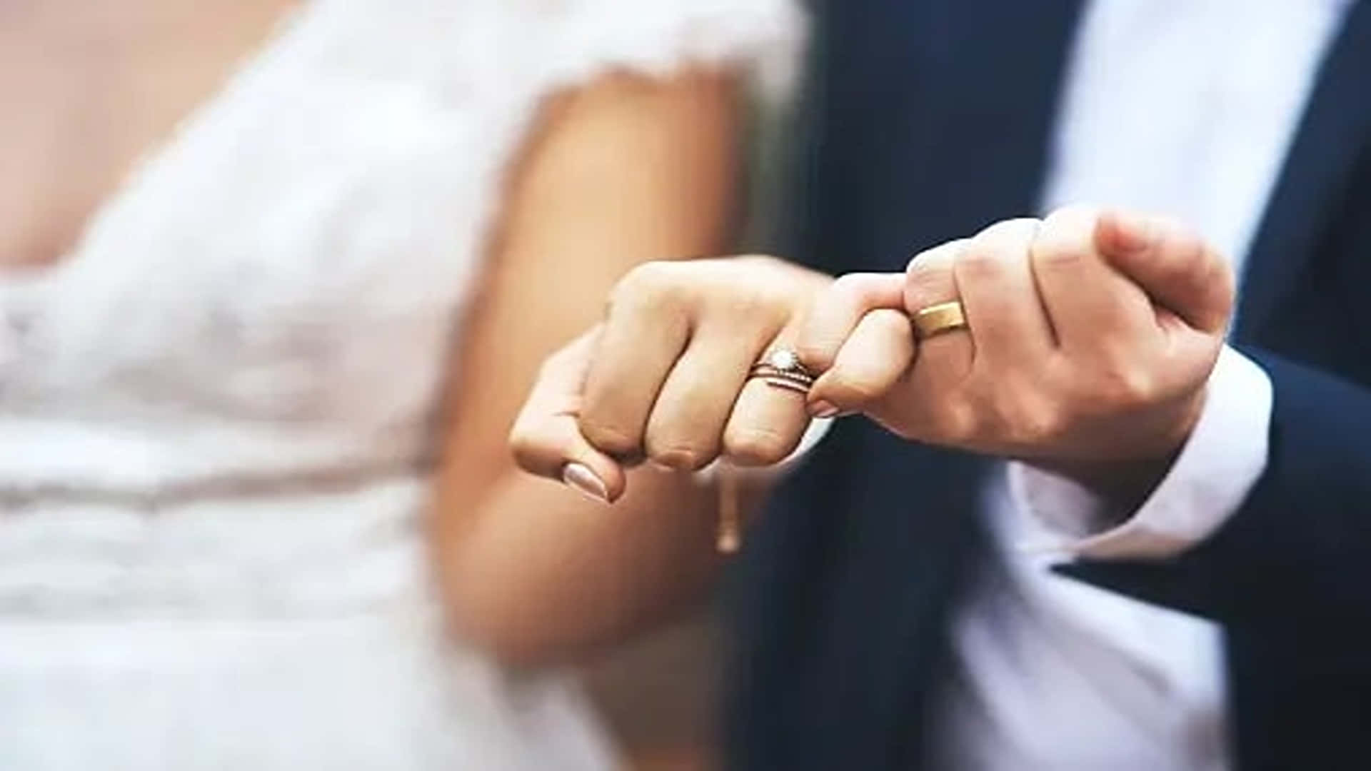 Eternal Life 桌布 壁紙 — 新郎新娘手指交扣的特寫，結婚戒指在溫暖燈光下柔和發光。