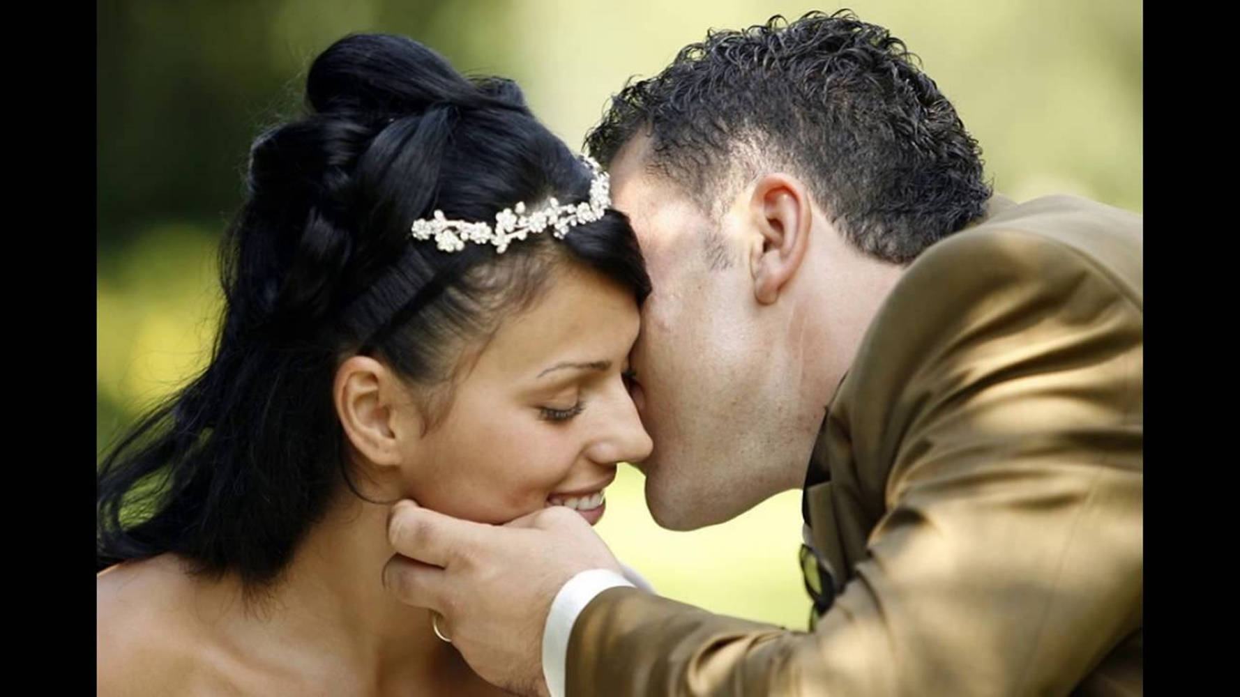 couples kissing 桌布 壁紙 — 新郎溫柔地親吻新娘的臉頰，新娘在陽光灑落的花園中輕柔微笑。