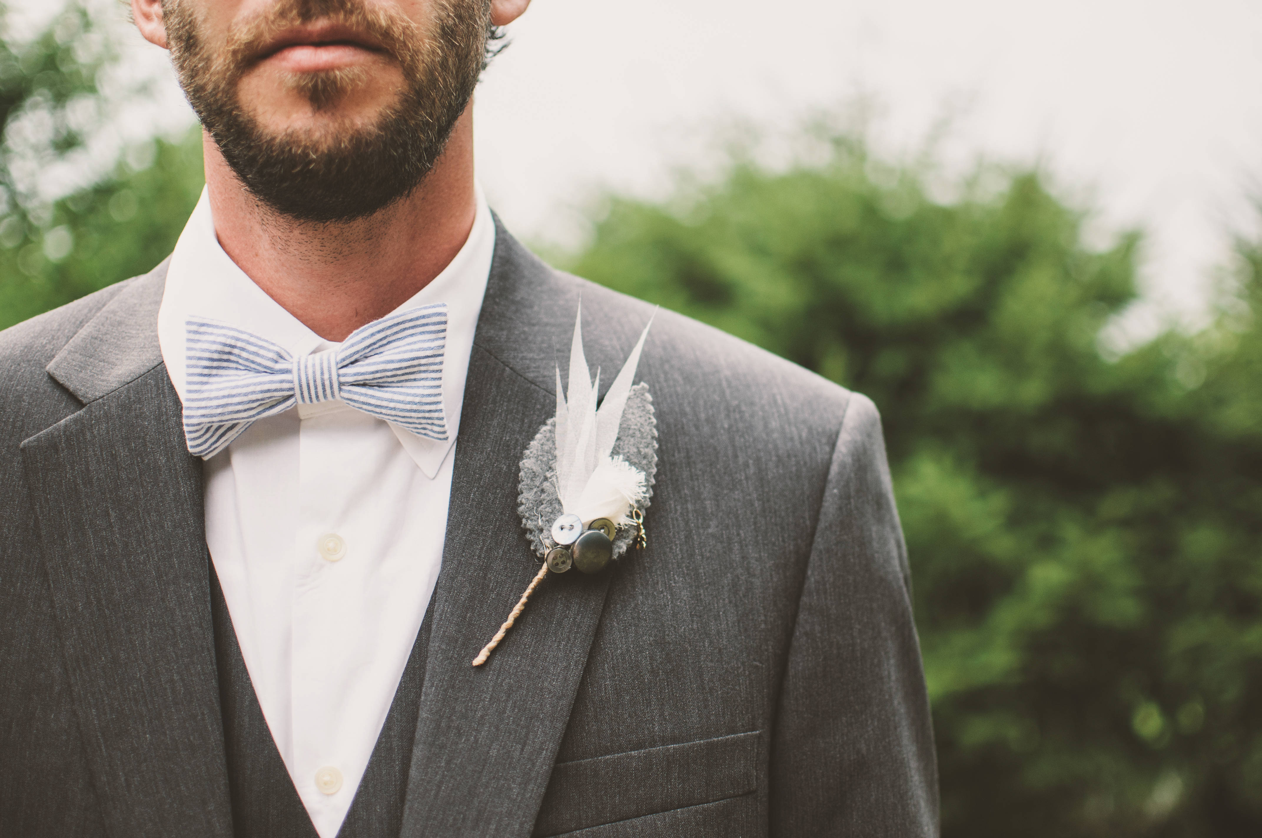 Groom 桌布 壁紙 — 新郎近照，身穿灰色西裝，搭配條紋蝴蝶結領結和羽毛襟花，背景是模糊的綠植。