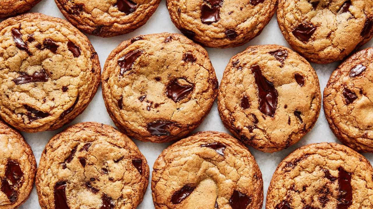 720p Cookies 桌布 壁紙 — 新鮮出爐的巧克力餅乾，金黃色邊緣和融化巧克力塊排列在烘焙紙上。