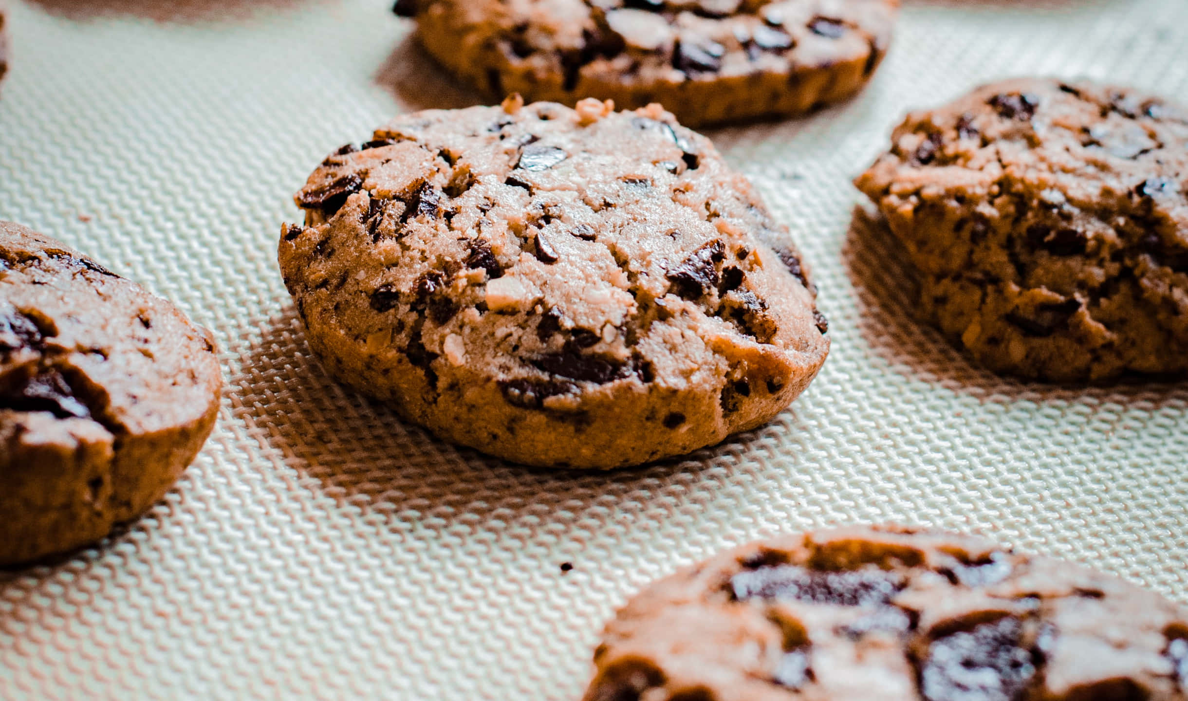 Cookies 桌布 壁紙 — 新鮮出爐的巧克力餅乾，金黃邊緣，放在有紋理的烘焙墊上。