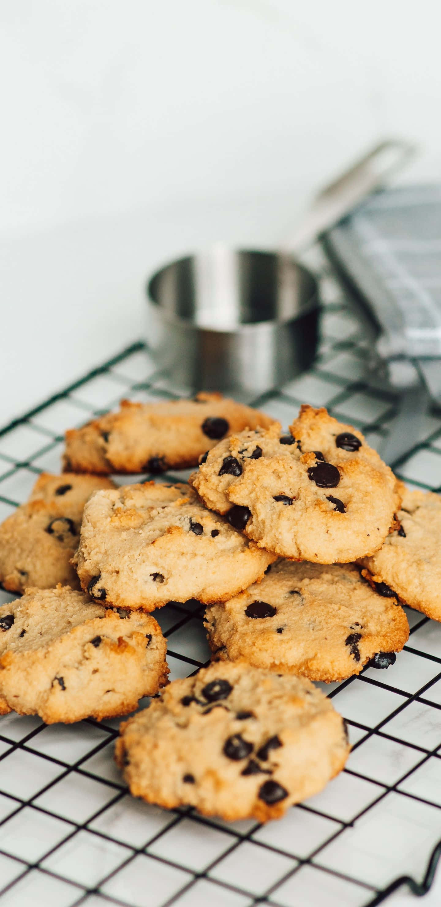 Pixel 3xl Cookies 桌布 壁紙 — 新鮮出爐的巧克力餅乾在金屬架上冷卻，旁邊有金屬勺和條紋毛巾。