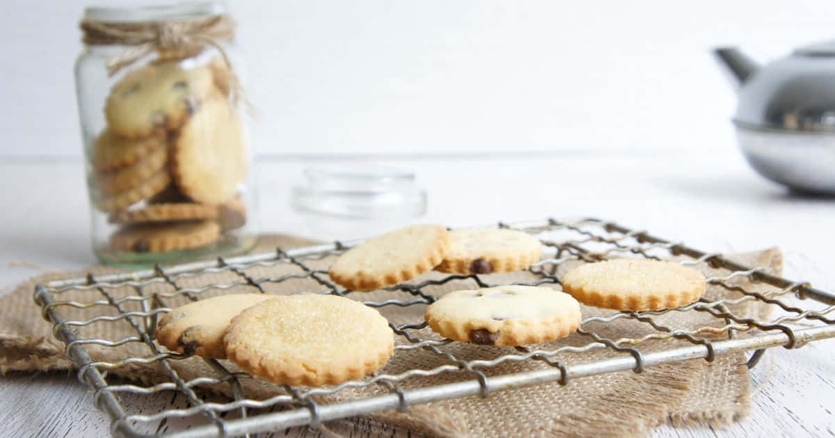 Biscuit 桌布 壁紙 — 新鮮出爐的巧克力餅乾在金屬架上冷卻，旁邊有一個裝滿更多餅乾的玻璃罐和一個銀茶壺。